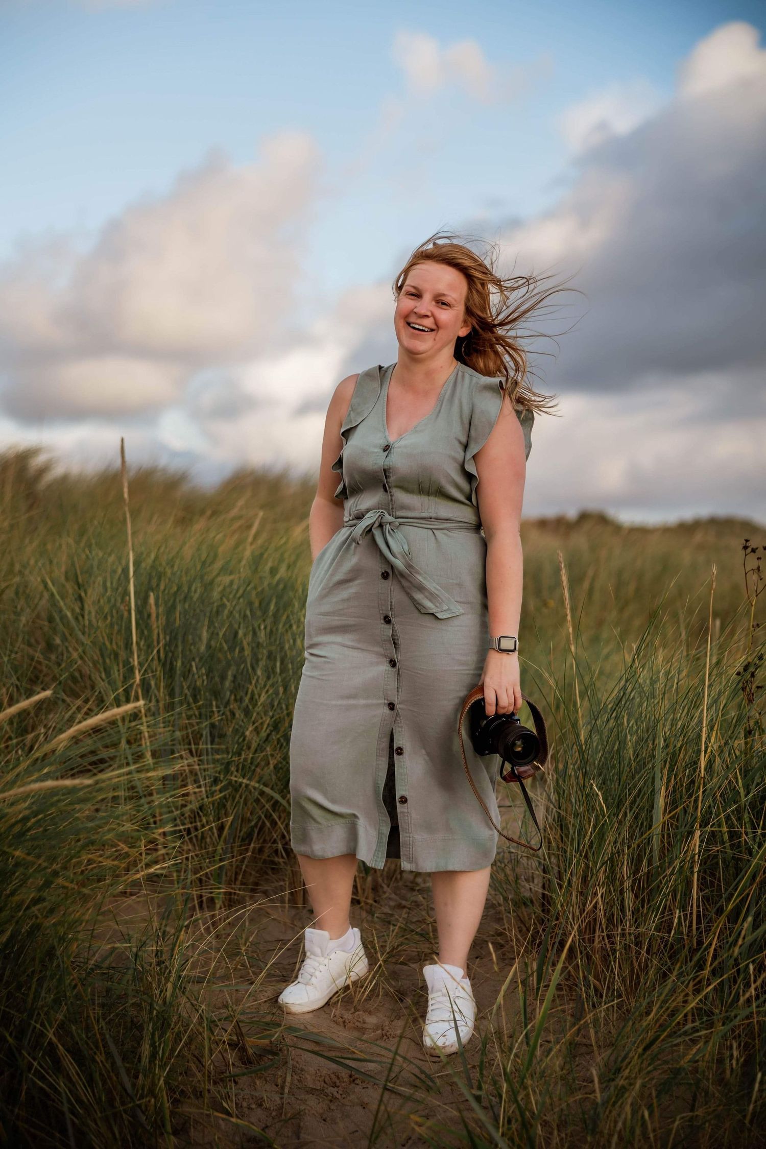 Photographer in casual grey outfit walking through tall grass on sunny day.