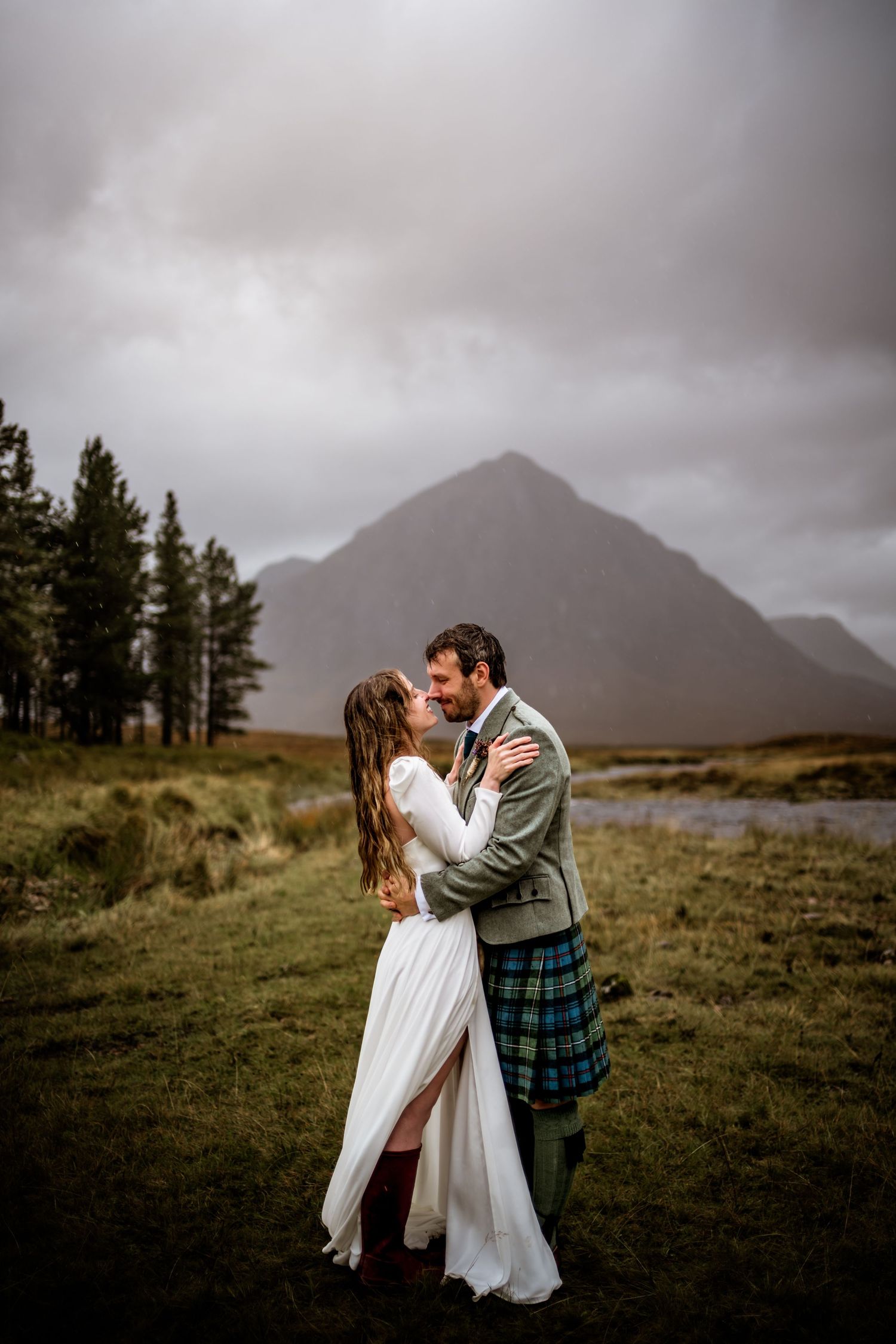 A wedding couple embraces on a hillside with dramatic mountain scenery in the background. Kings House Hotel Wedding Photography