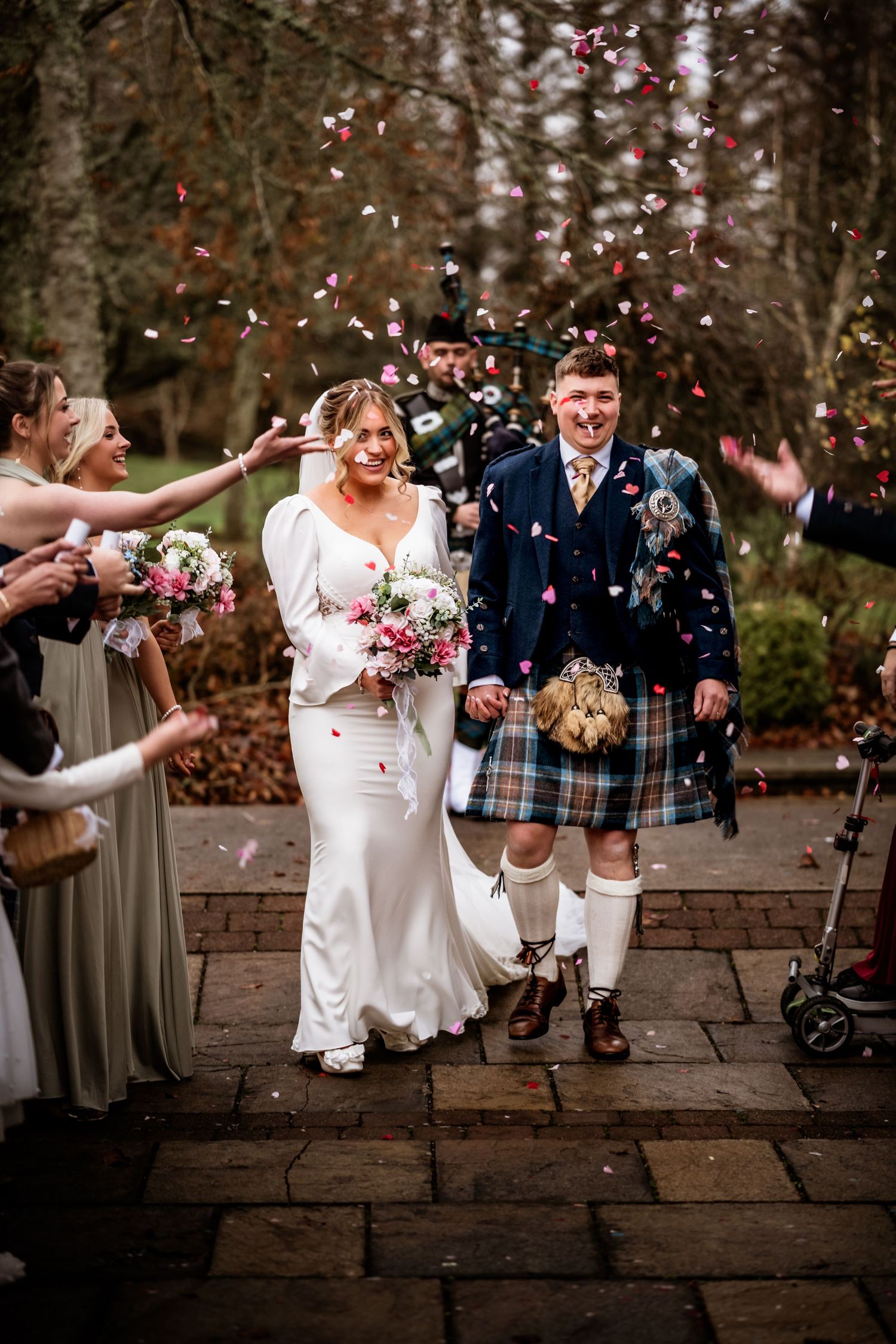 Guests shower the newlyweds with confetti as they walk down a stone pathway.
