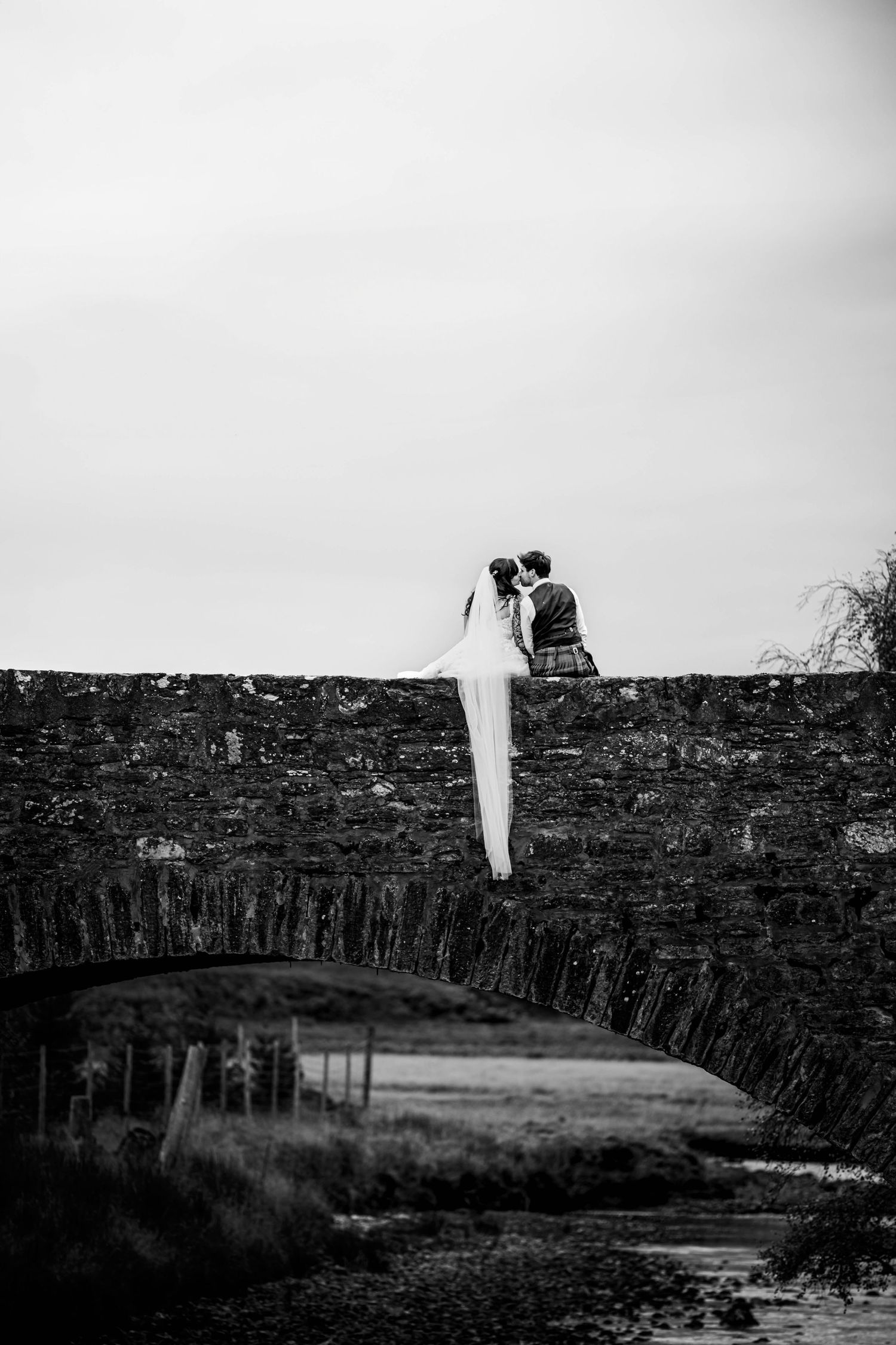 Silhouetted couple standing on ancient stone wall against moody sky. Scottish Highlands Achnasheen Wedding photography