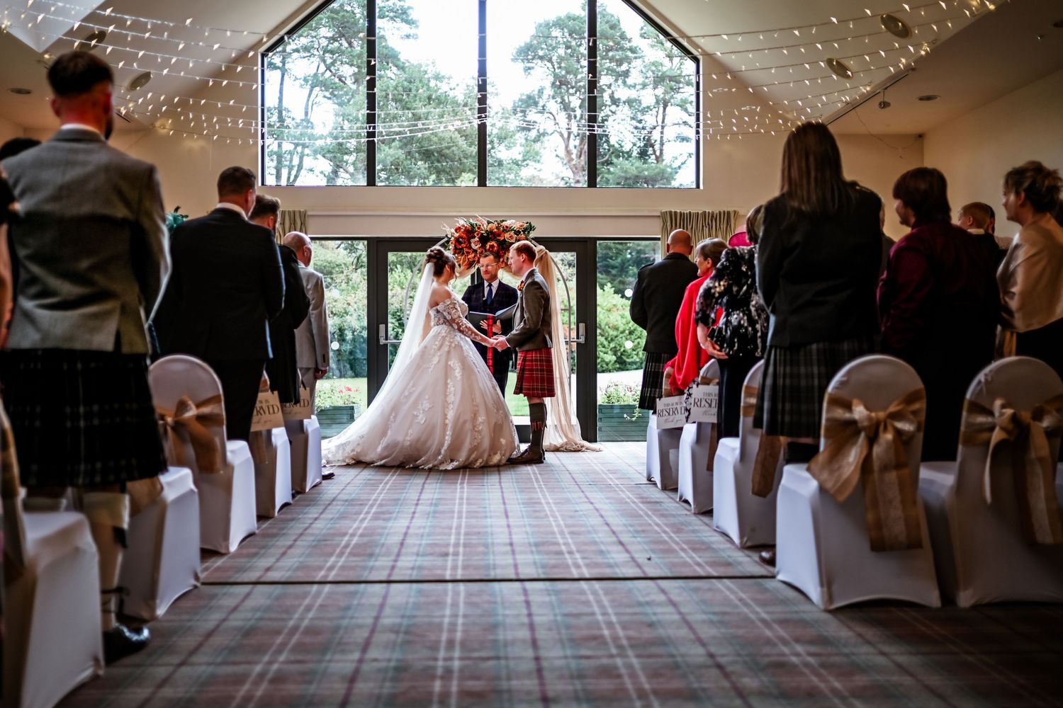 Wedding ceremony venue decorated with white chairs and string lights creating a romantic atmosphere. LochNess Country House Hotel Wedding