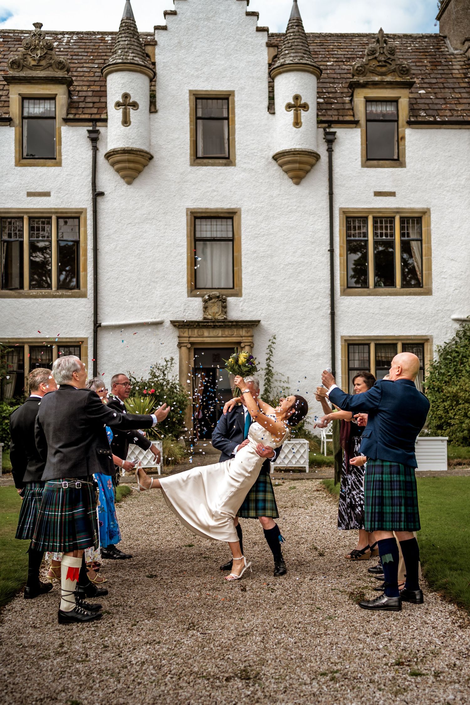 Traditional Scottish wedding celebration with guests in kilts dancing on the grounds of a historic white building. Scottish Highlands
