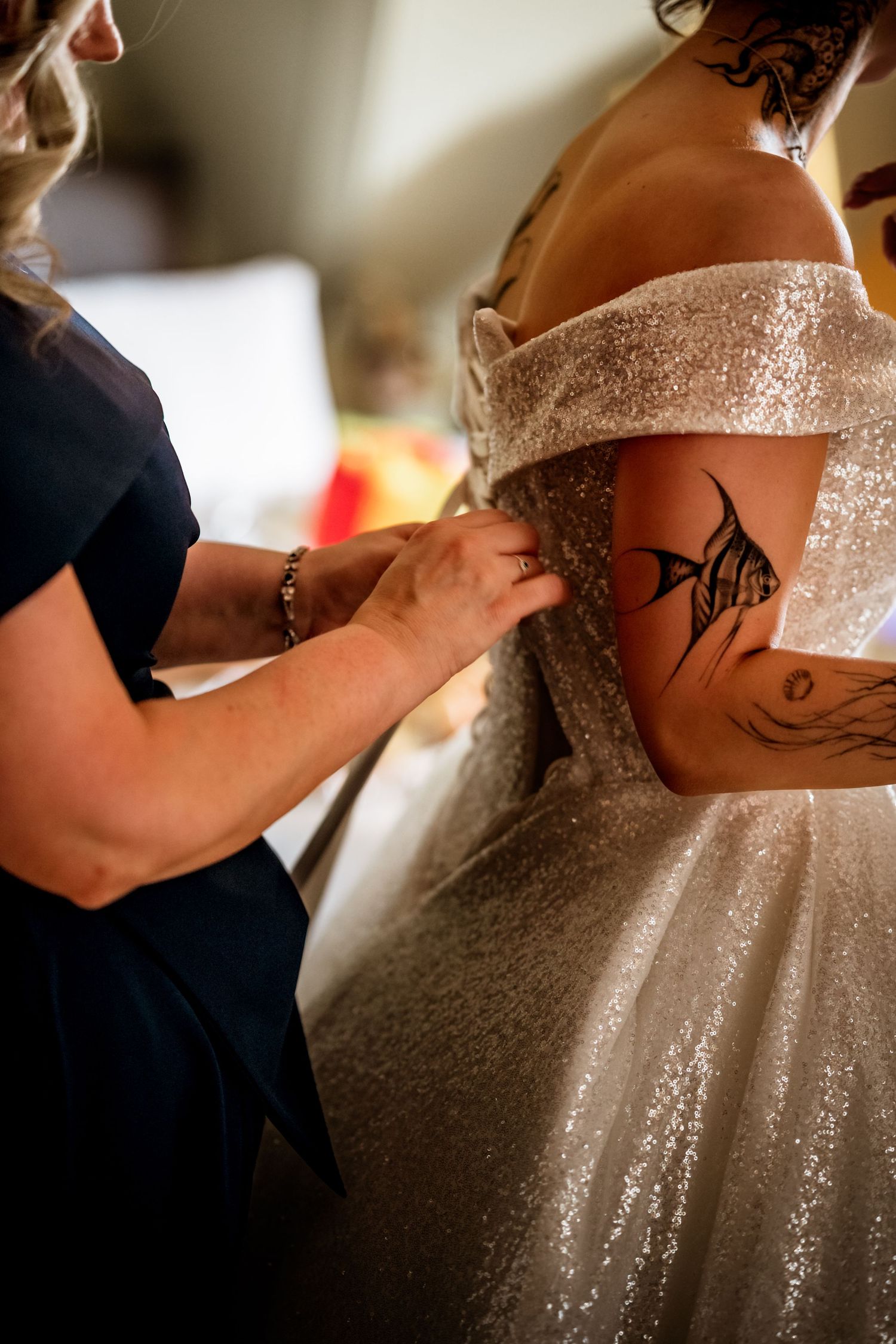 A close-up shot of a sparkly wedding dress being adjusted, with a visible tattoo on the wearer's arm. Scottish Highlands Inverness Wedding