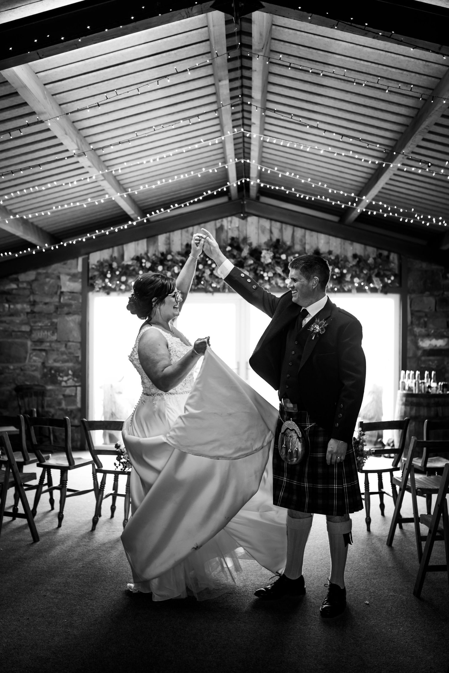 A couple dancing under twinkling lights, with the groom wearing a traditional Scottish kilt.