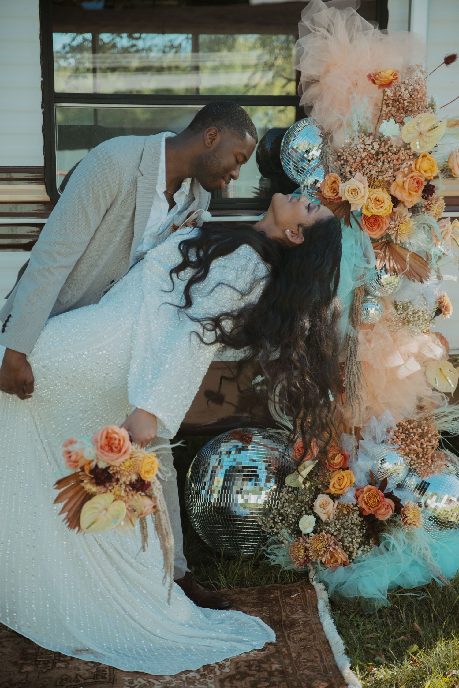 Couple nearly kissing beside a floral arch with disco balls and orange roses in Northern and Central Minnesota.