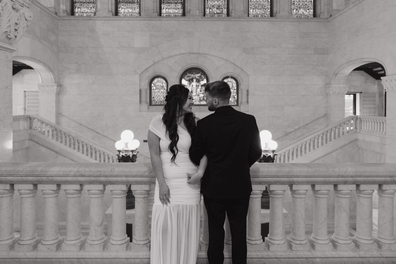 Black and white photo of bride and groom facing grand staircase in elegant Minneapolis City Hall.
