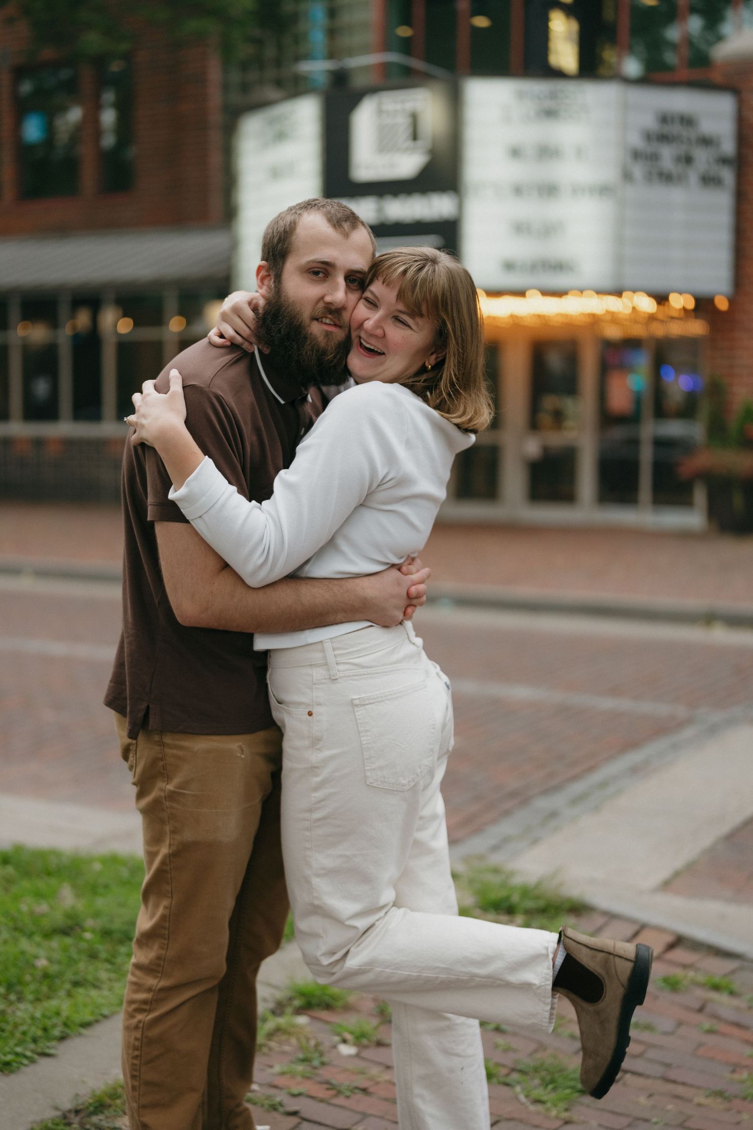 Happy couple embraces and laughs outside vintage theater marquee on brick city street near Saint Anthony Main in Minneapolis, Minnesota.