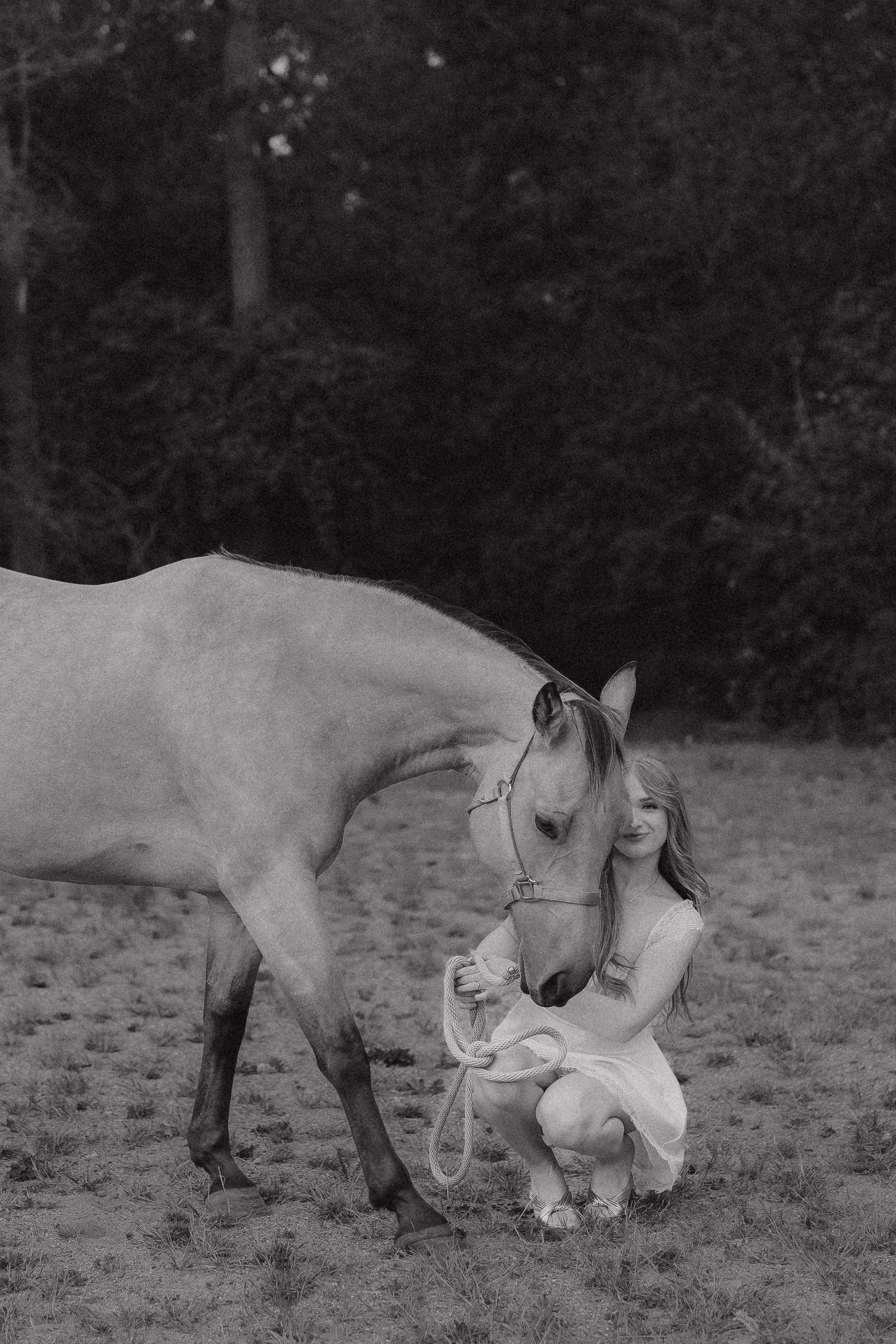 Black and white photo of a young woman in white dress crouching beside a horse in Minnesota.
