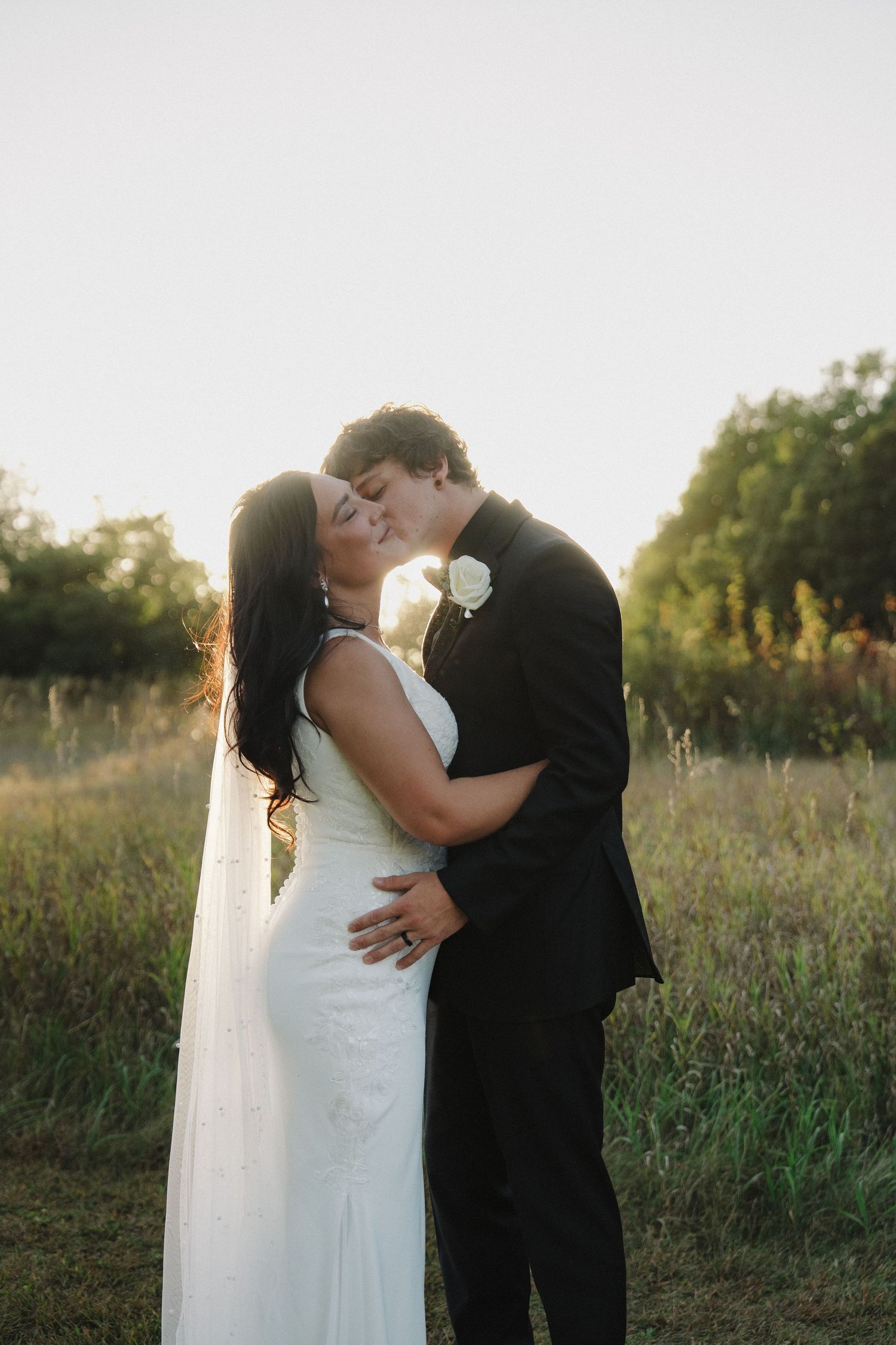 Bride and groom sharing a romantic kiss in a golden sunlit meadow during their outdoor wedding near Mankato, Minnesota.