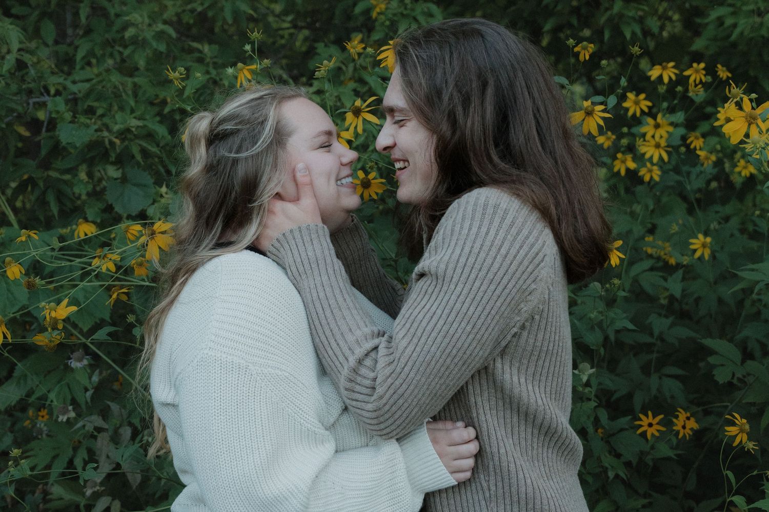 Young couple embracing and smiling at each other in front of yellow wildflowers at Lebanon Hills Regional Park in Eagan, Minnesota.