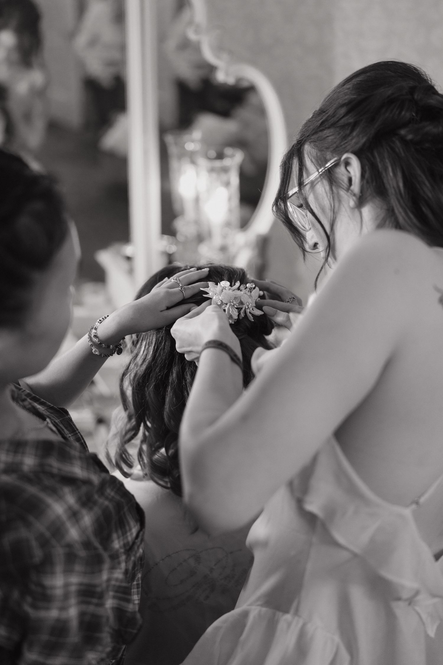 Black and white photo of two women placing floral crown on bride's hair during wedding preparation.