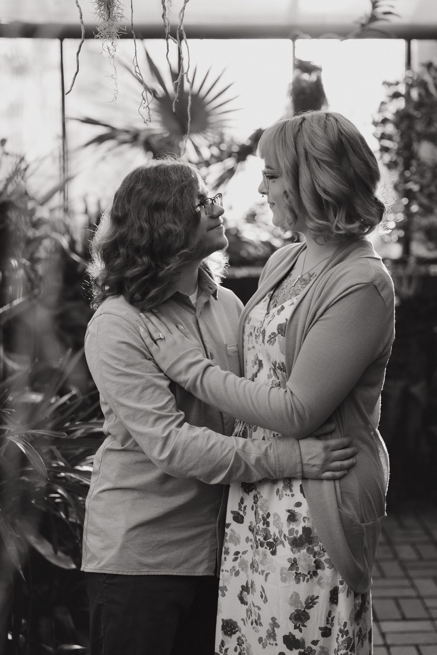 Black and white photo of two women embracing and smiling at each other in a greenhouse setting at the Minnesota Landscape Arboretum.