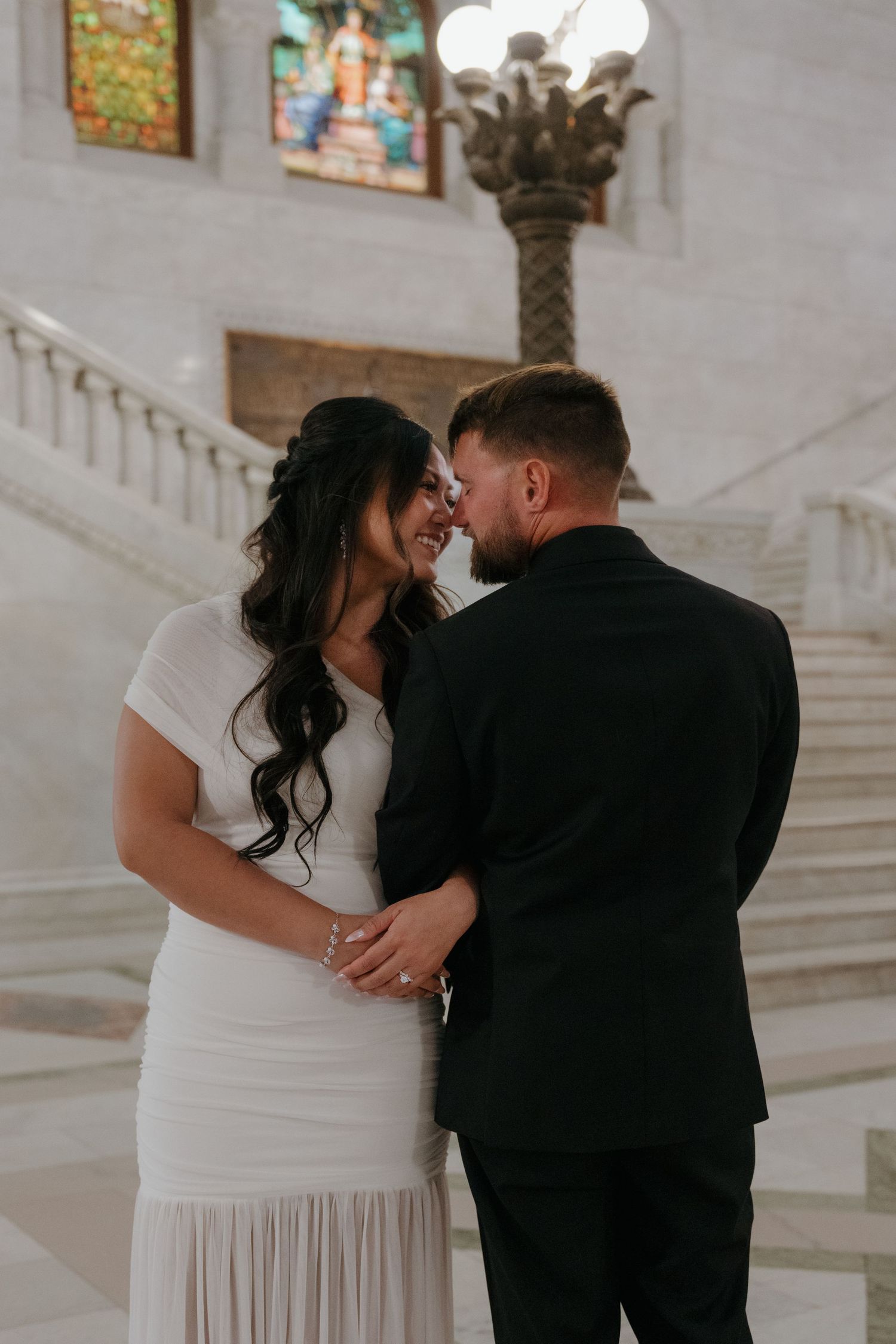 Bride and groom share intimate forehead touch inside elegant marble building with stained glass at Minneapolis City Hall.