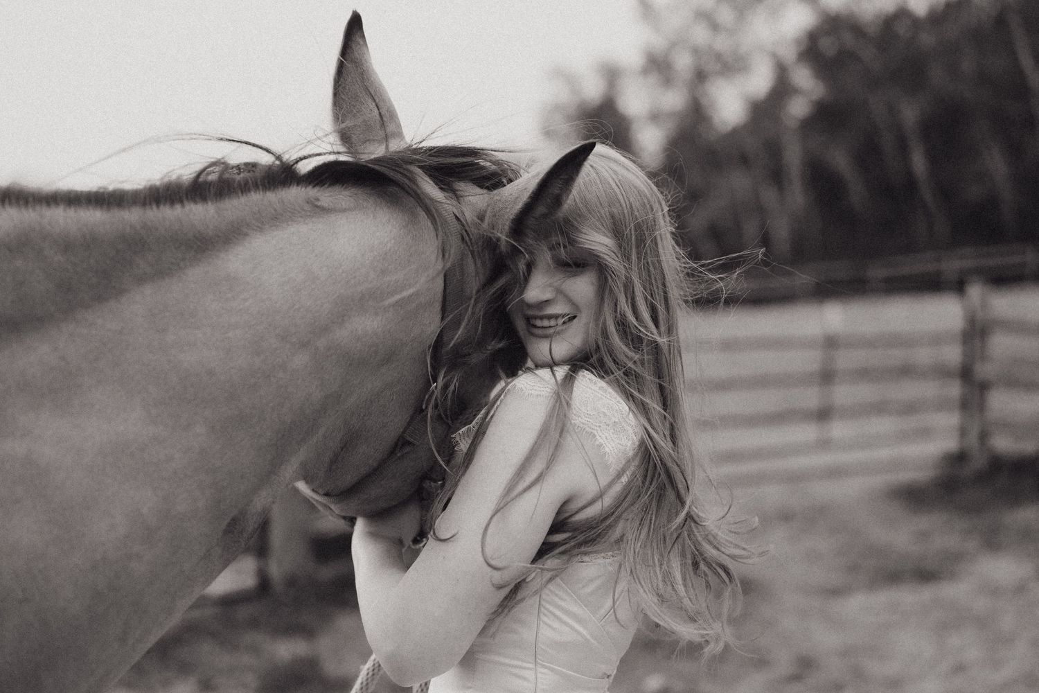 Black and white photo of smiling bride embracing a horse outdoors in Minnesota.