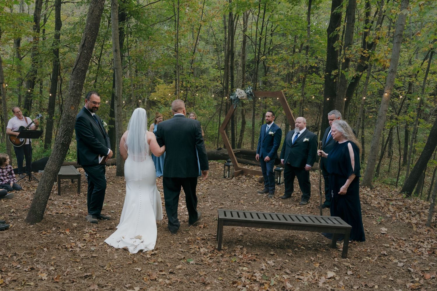 Small intimate outdoor wedding ceremony in autumn forest with wedding party and guests gathered for a backyard wedding in Shakopee, MN.