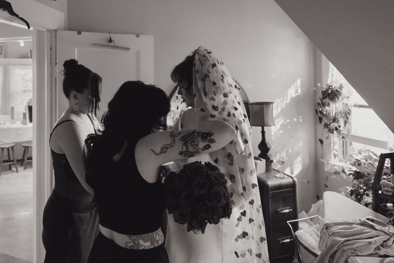 Black and white photo of bridesmaids helping bride with her floral veil before the wedding ceremony in Longfellow of Minneapolis, Minnesota.