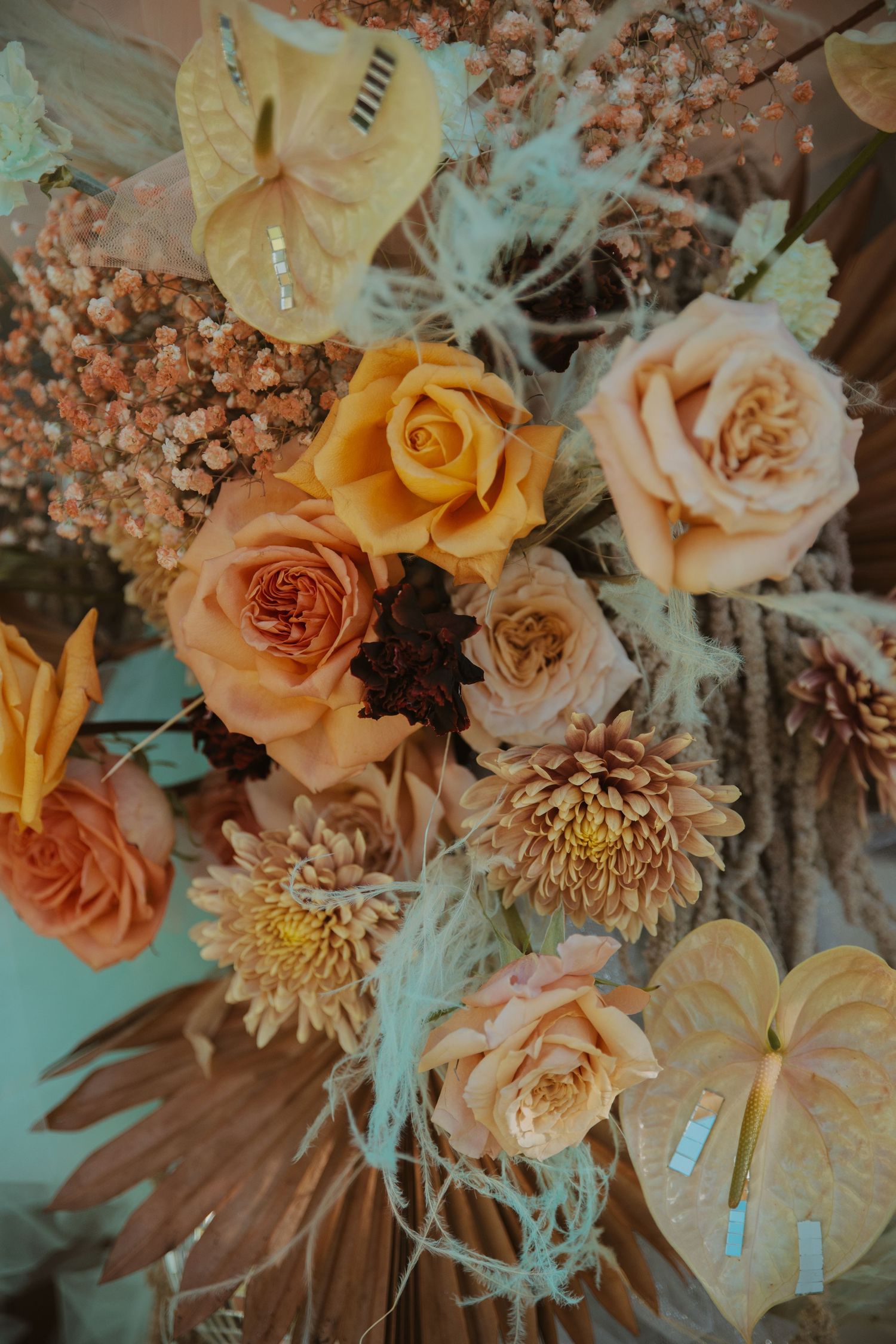 A lush arrangement of orange, peach, and yellow roses with dahlias and dried botanicals with a vintage aesthetic.