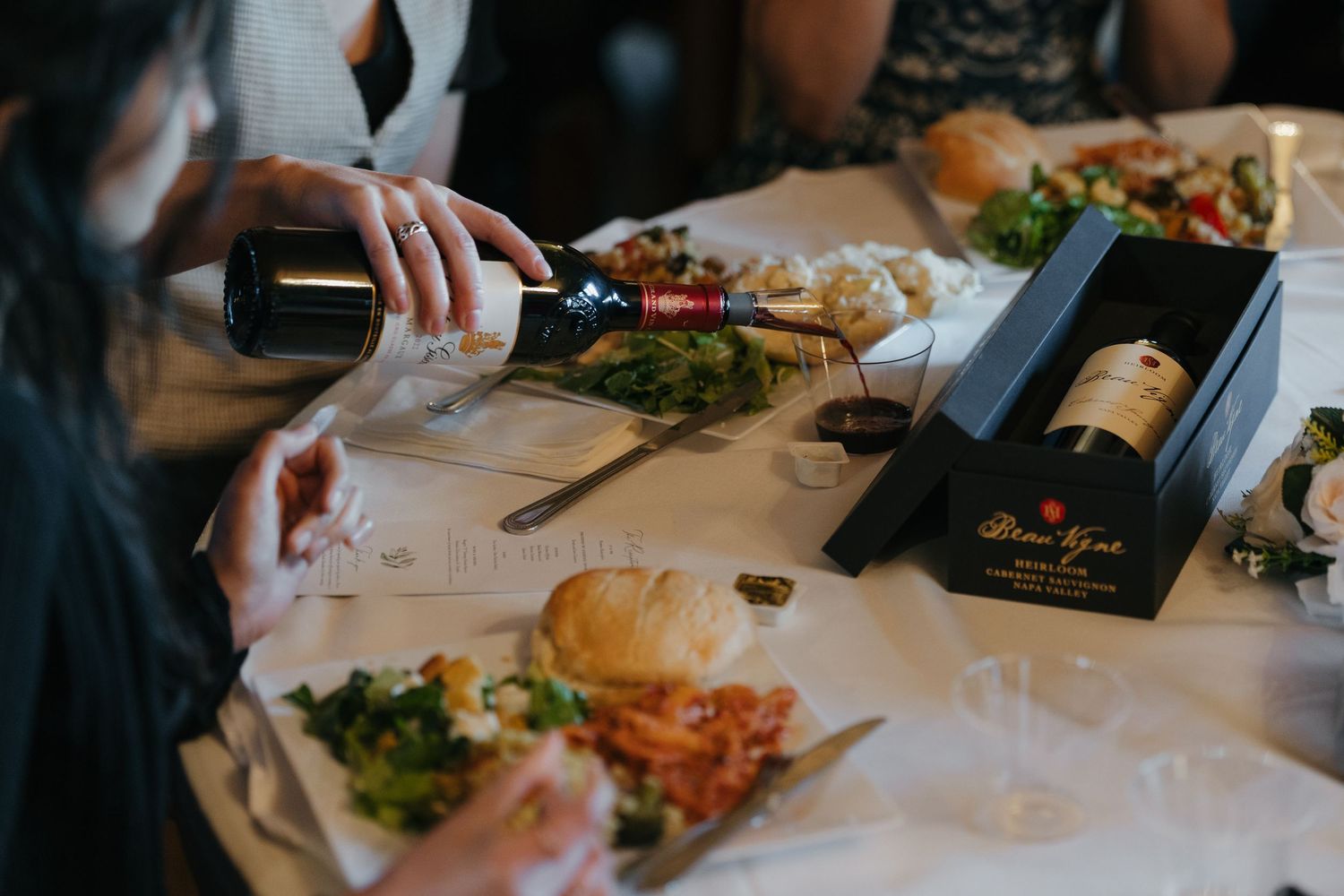 Guest pouring red Beau Vigne wine at a dinner table with salads and bread rolls in Rochester, Minnesota at the historic Plummer House.