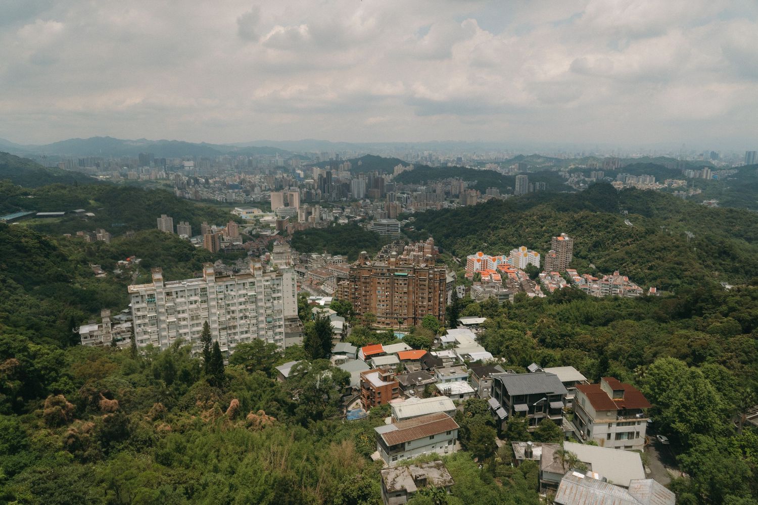 Aerial view of a hillside residential neighborhood surrounded by dense green forests in Taipei, Taiwan.