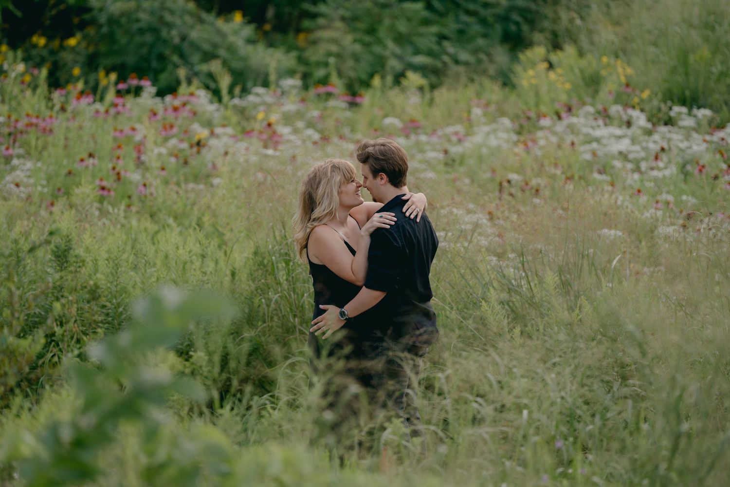 Romantic couple embraces and kisses surrounded by lush wildflowers in a vibrant summer meadow at Schaar's Bluffs in Hastings, Minnesota.