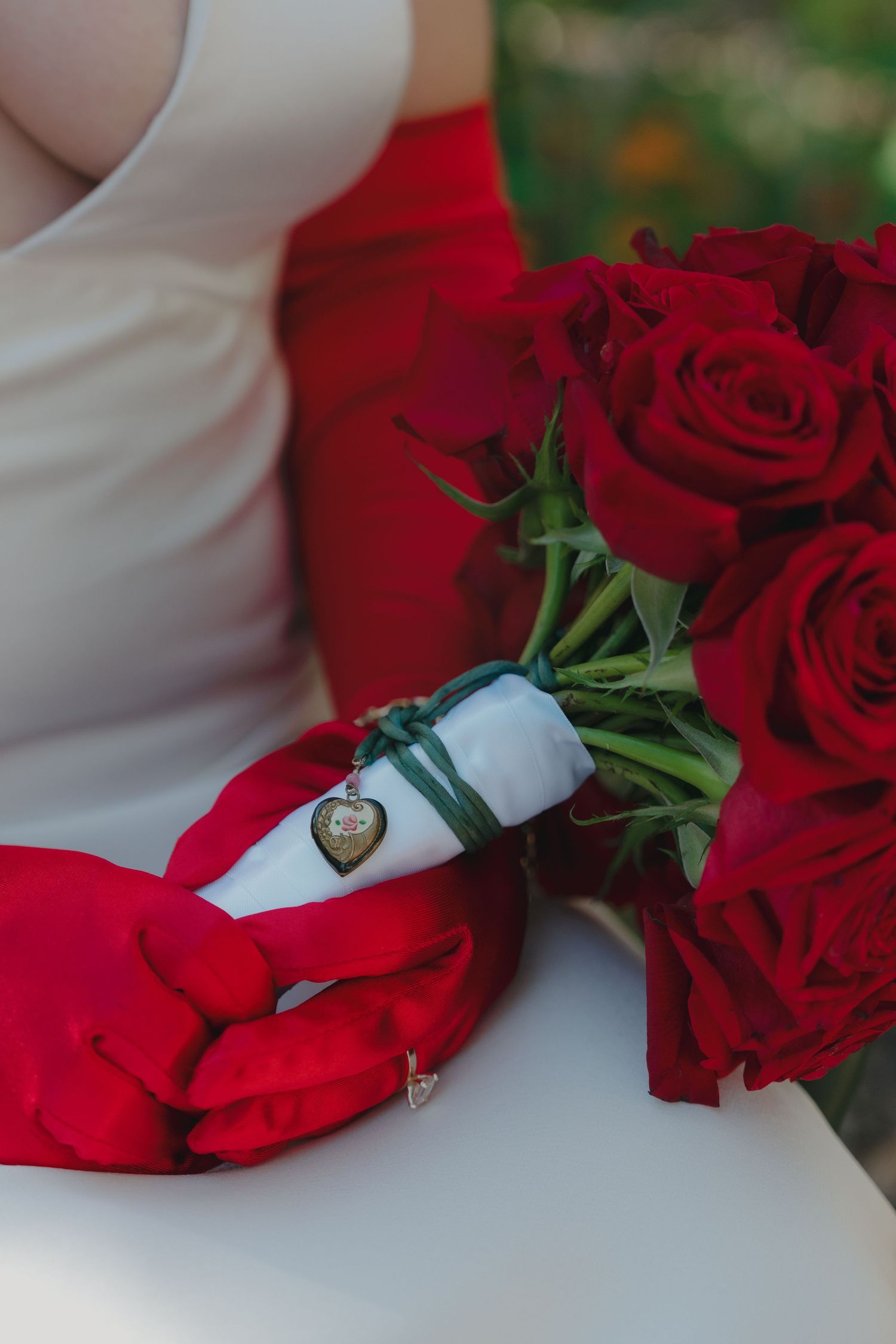 Bride in white dress with red gloves holding a red rose bouquet with a decorative heart locket charm in Minnesota.