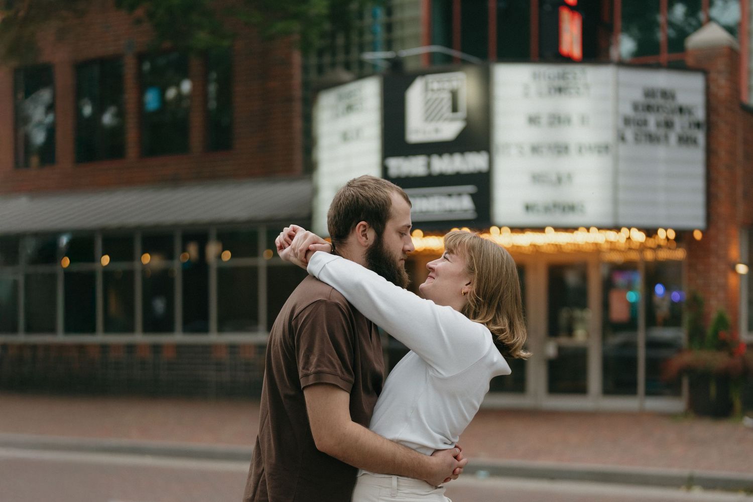 Couple embracing romantically in front of a lit theater marquee at dusk off Saint Anthony Main in Minneapolis.