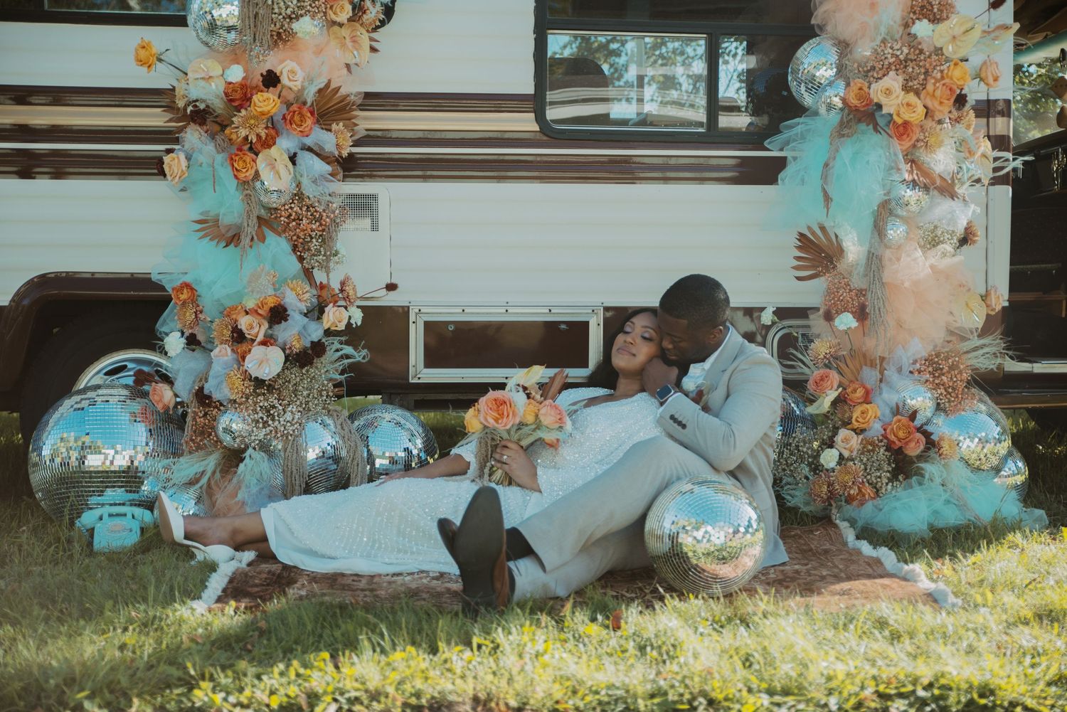 A couple sits together in front of an RV decorated with teal balloons and orange floral arrangements in North Shore, Minnesota area.