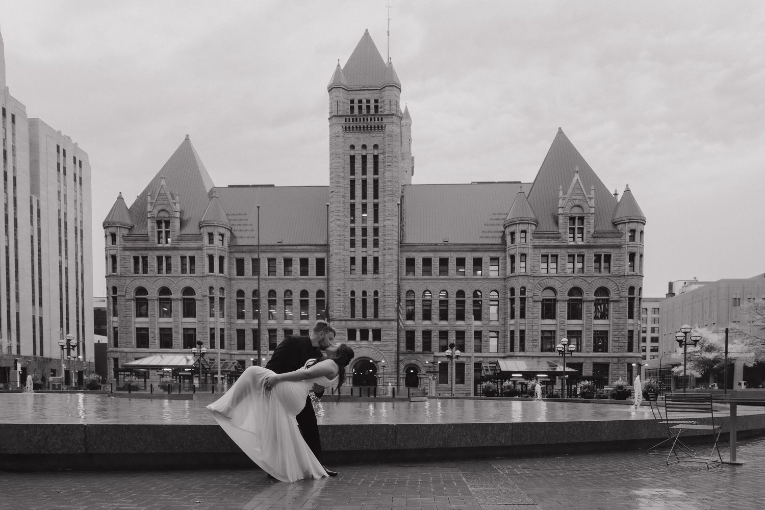 Black and white photo of a couple sharing a romantic dip kiss outside a grand historic building on their wedding day.