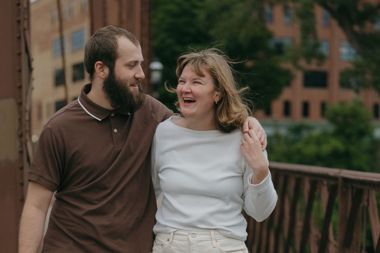 Happy couple laughing together on a bridge with urban buildings in the background on a windy day near Saint Anthony Main in Minneapolis.
