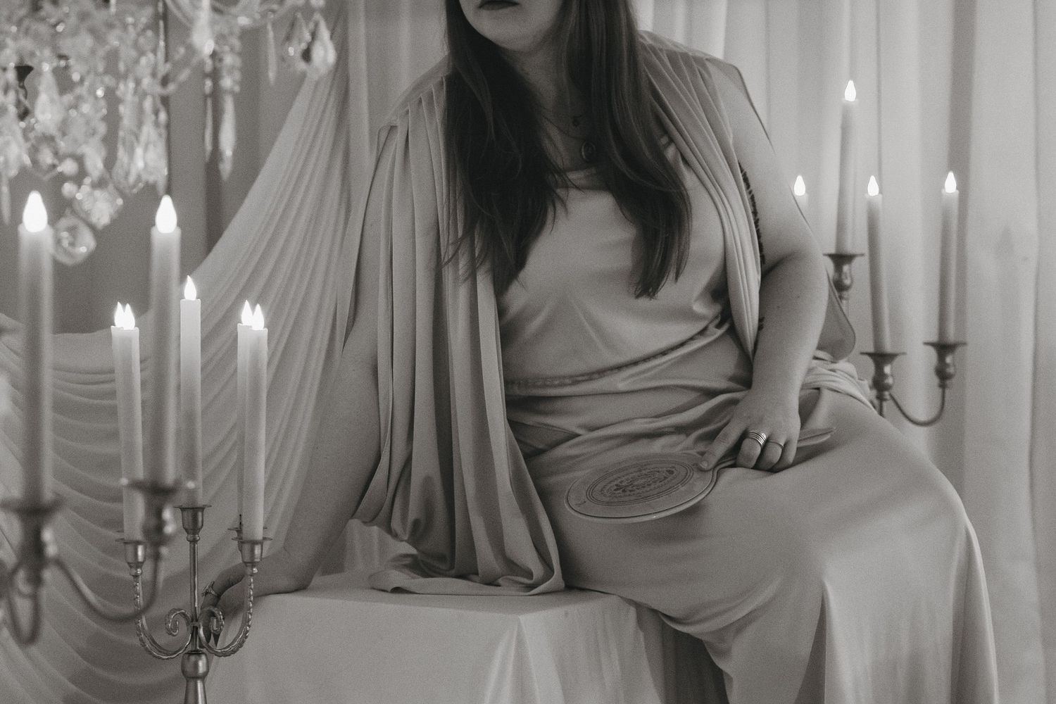 Black and white artistic portrait of woman in draped gown seated among glowing candelabras at a studio in Saint Paul, Minnesota.