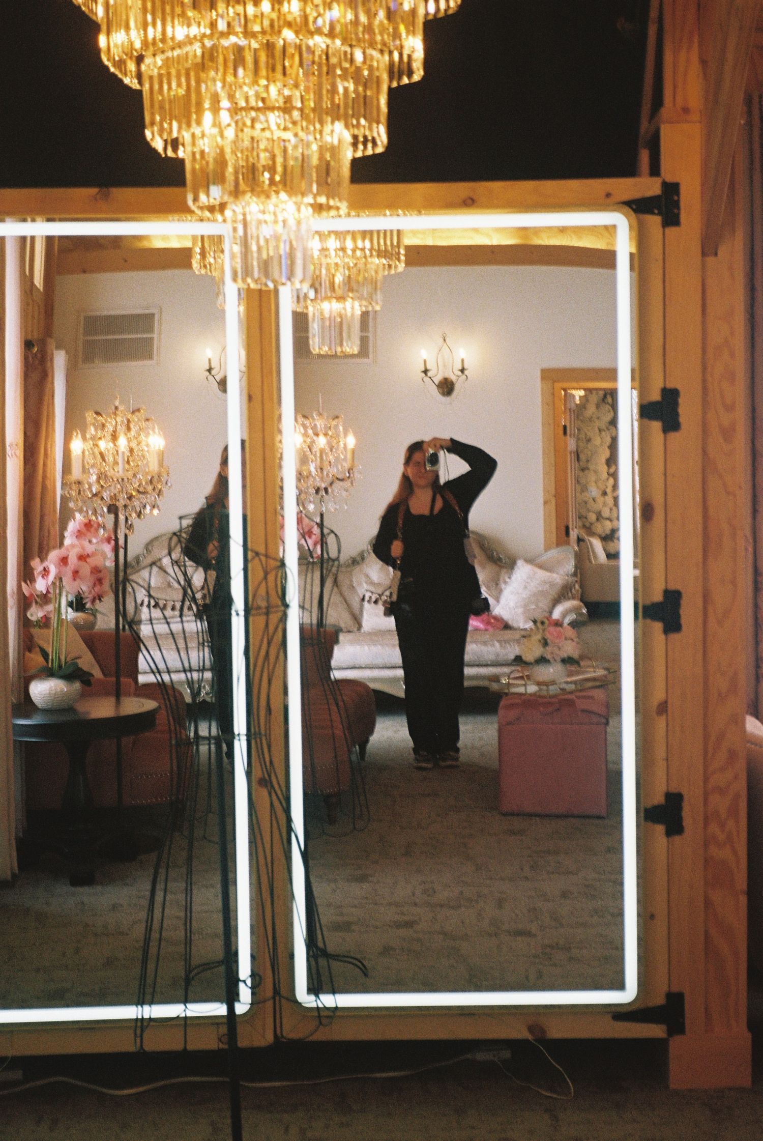 Woman taking a mirror selfie in an elegant room with a gold chandelier reflection at a Isanti wedding venue in Minnesota.