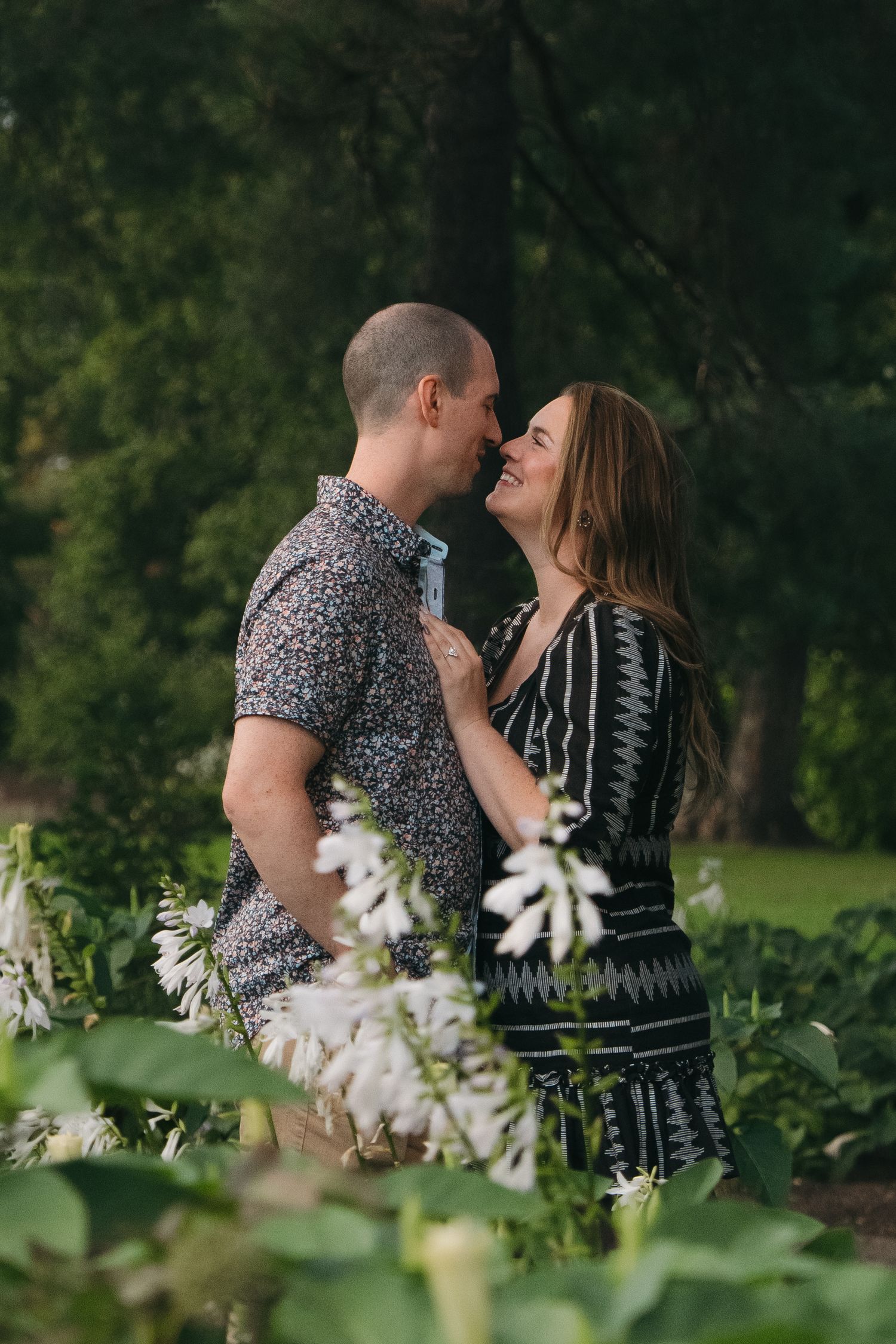 Romantic couple nearly kissing while embracing in a lush green garden with white flowers at Como Conservatory gardens in Saint Paul, MN.