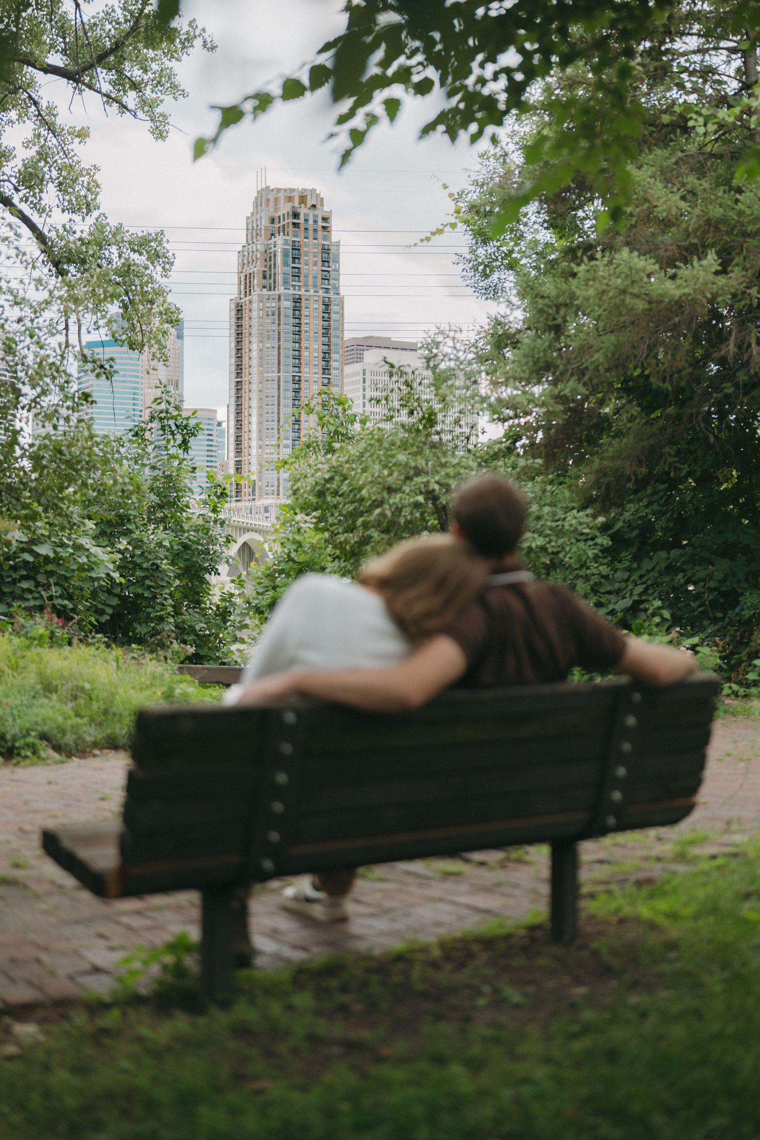 Couple sitting on a park bench overlooking a city skyline surrounded by lush green trees in Minneapolis, Minnesota.