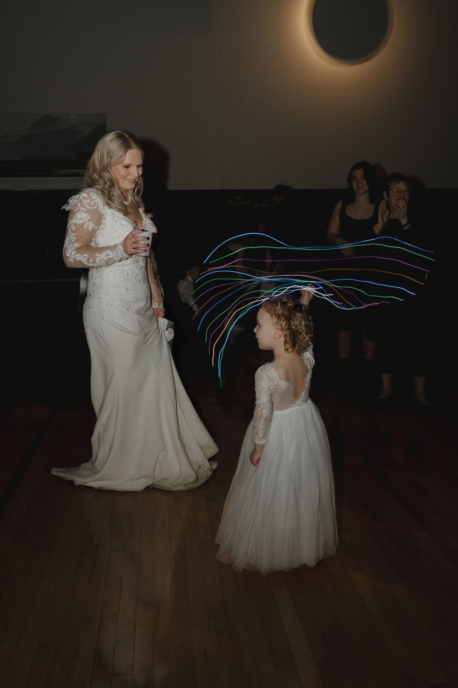 Bride in lace wedding gown dancing with flower girl waving colorful light wand at wedding reception in the Twin Cities, Minnesota.