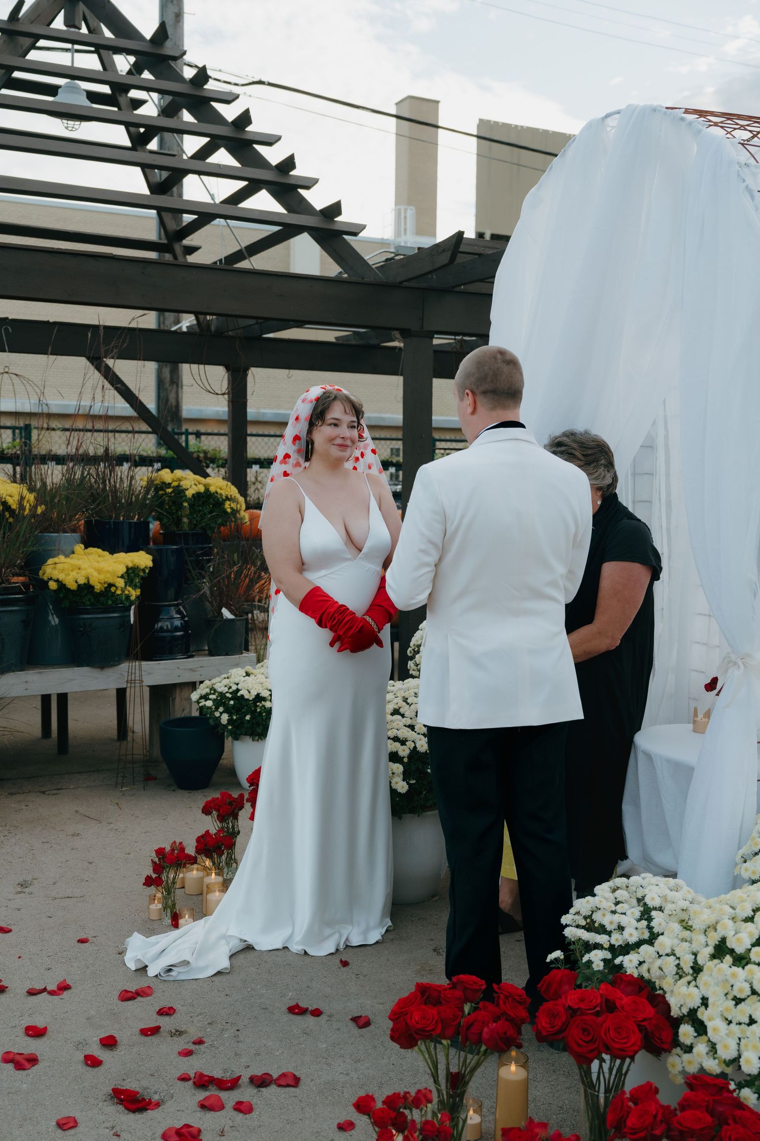 Bride in white gown with red gloves exchanges vows with groom at floral garden ceremony inspired by a Las Vegas elopement in Minnesota.