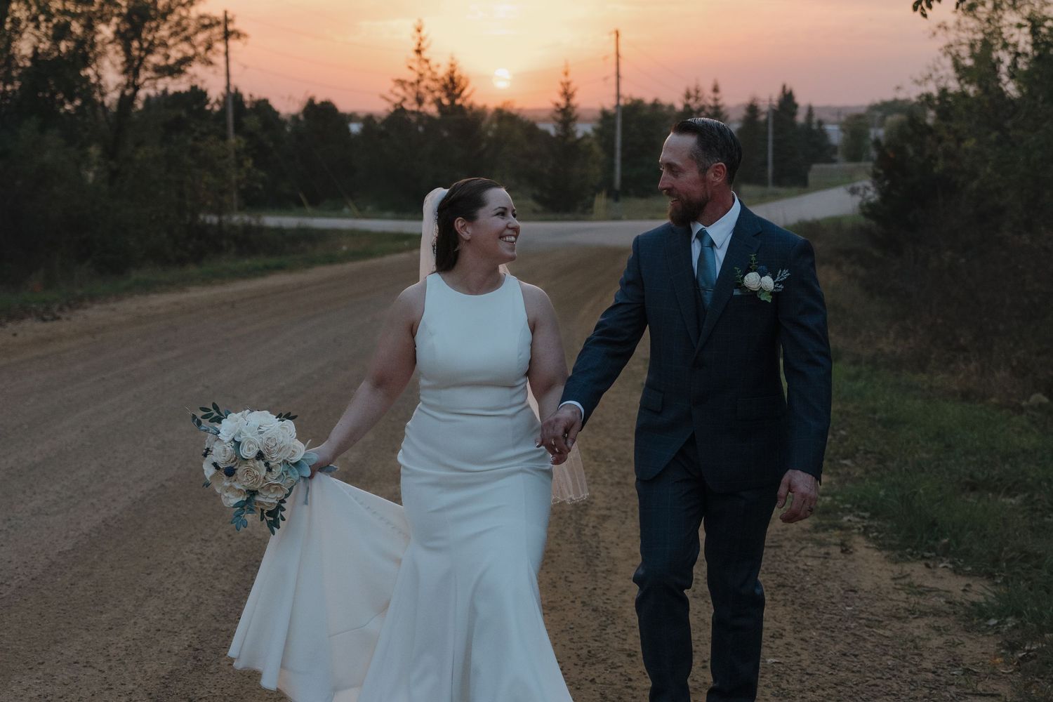 Bride and groom holding hands walking on a dirt road at sunset during their outdoor wedding in Southern Minnesota.
