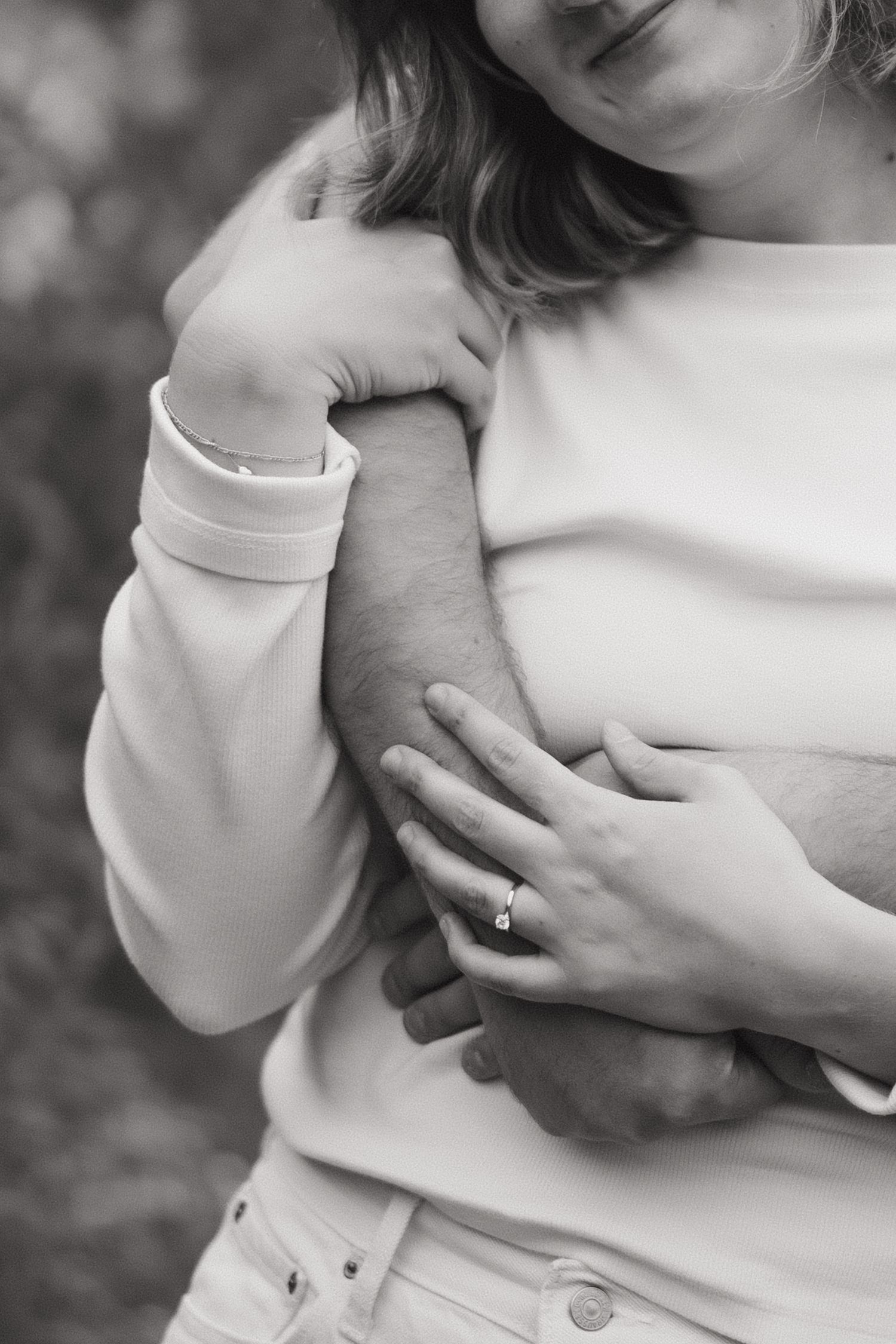 Black and white photo of a couple embracing, woman wearing an engagement ring holding man's arm tenderly.