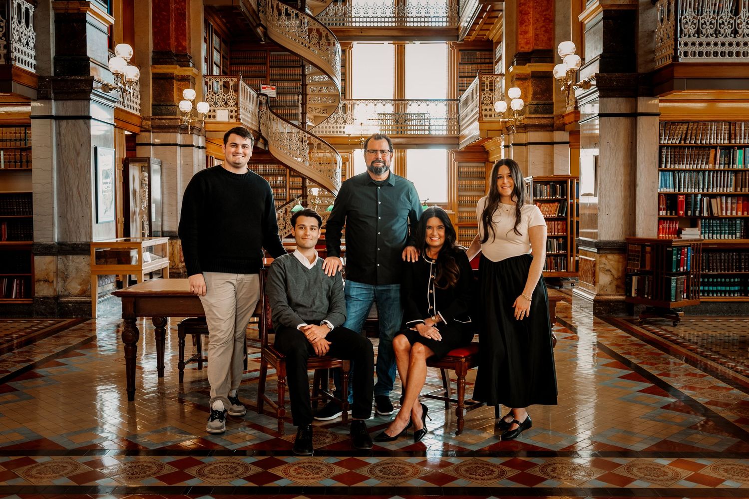 Family of five posing together in ornate historic library with grand staircase.