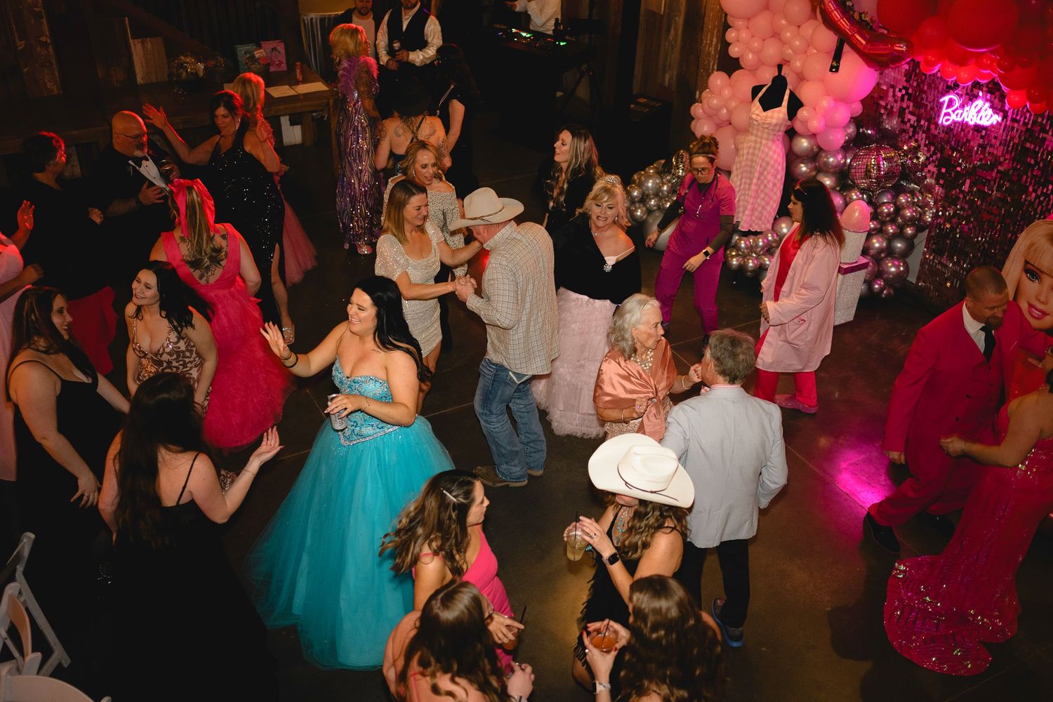 Guests dancing and celebrating at a vibrant wedding reception with pink lighting and festive decorations.
