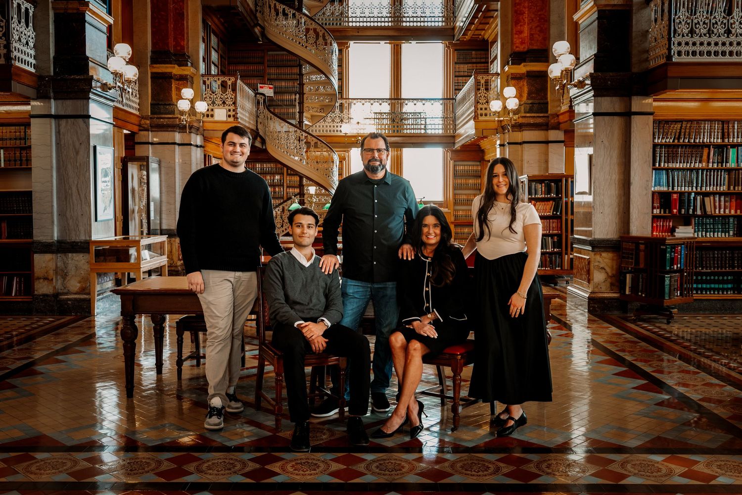 Family of five posing together inside an elegant historic library with ornate bookshelves.