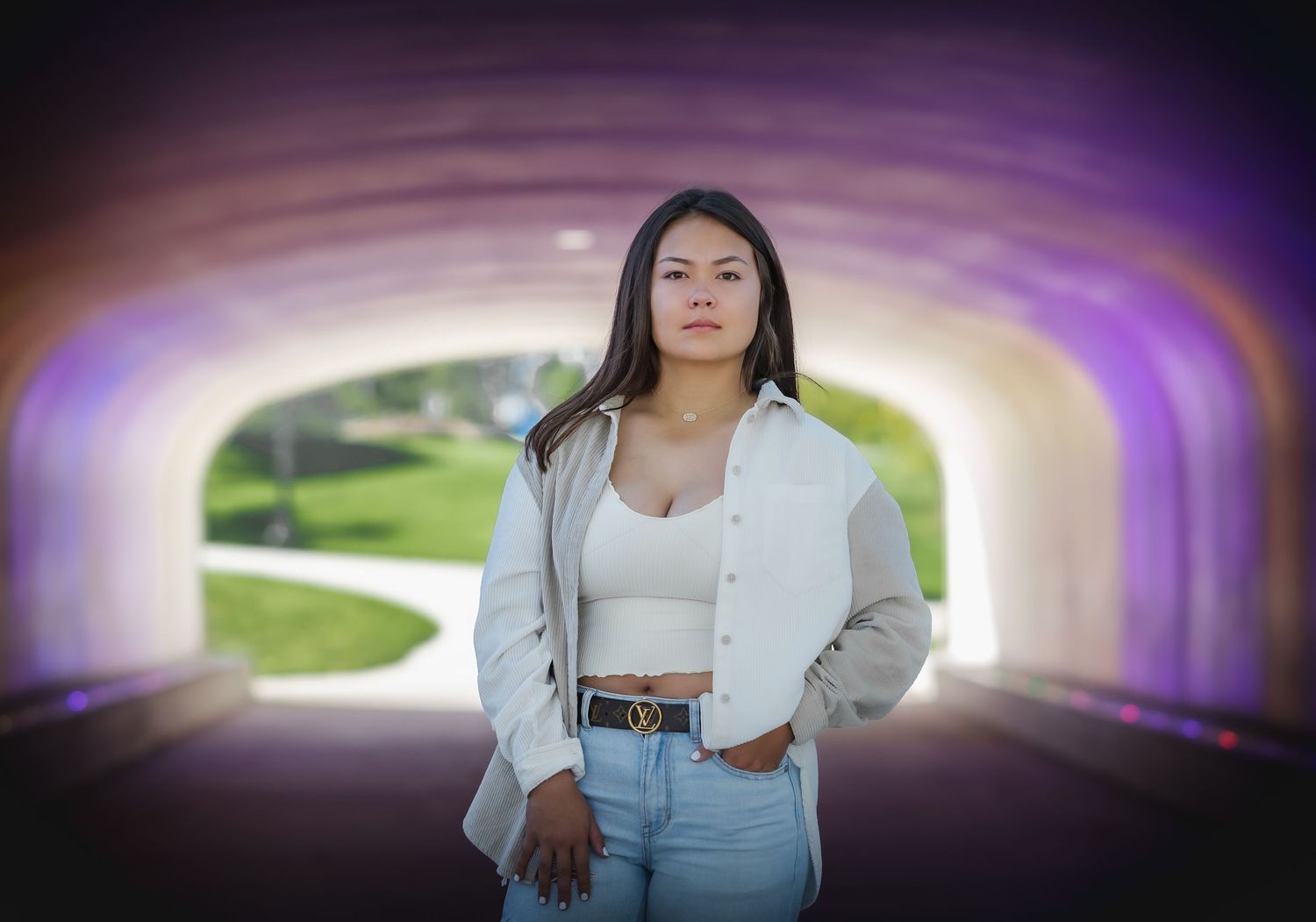 Young woman poses confidently in white outfit inside a glowing purple tunnel.