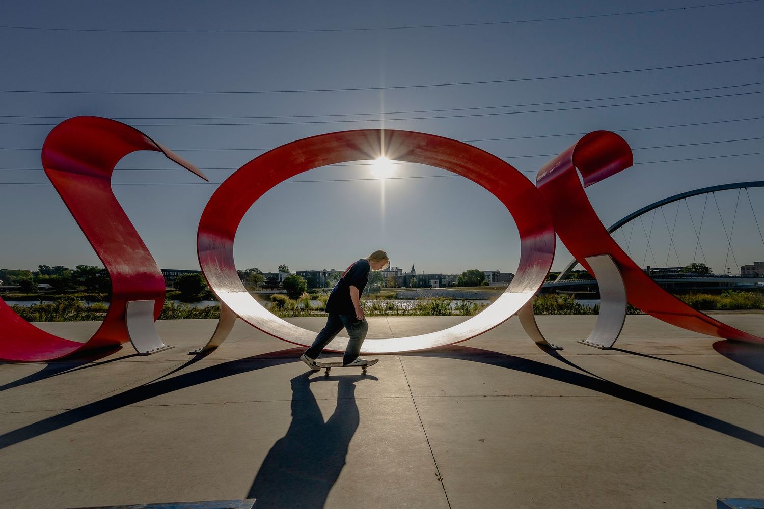 Skateboarder silhouetted through large red metal sculpture art installation outdoors.