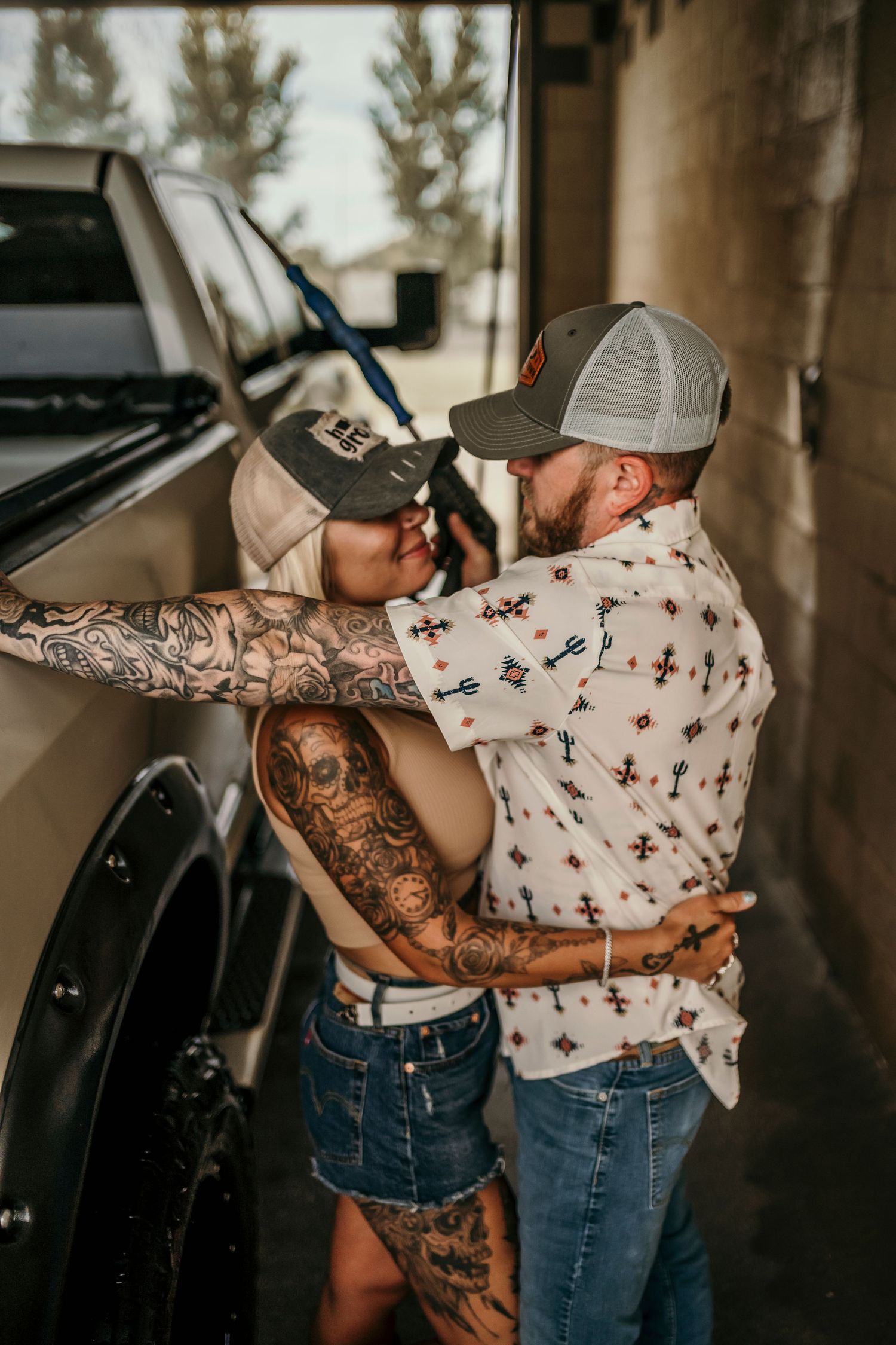 Tattooed couple sharing a romantic embrace near a truck at a car wash.