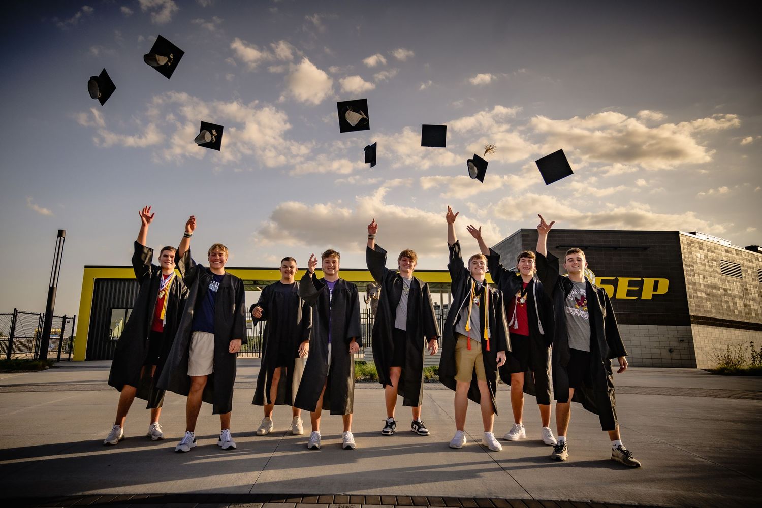 Group of graduates tossing caps in the air outdoors at sunset in front of a building.