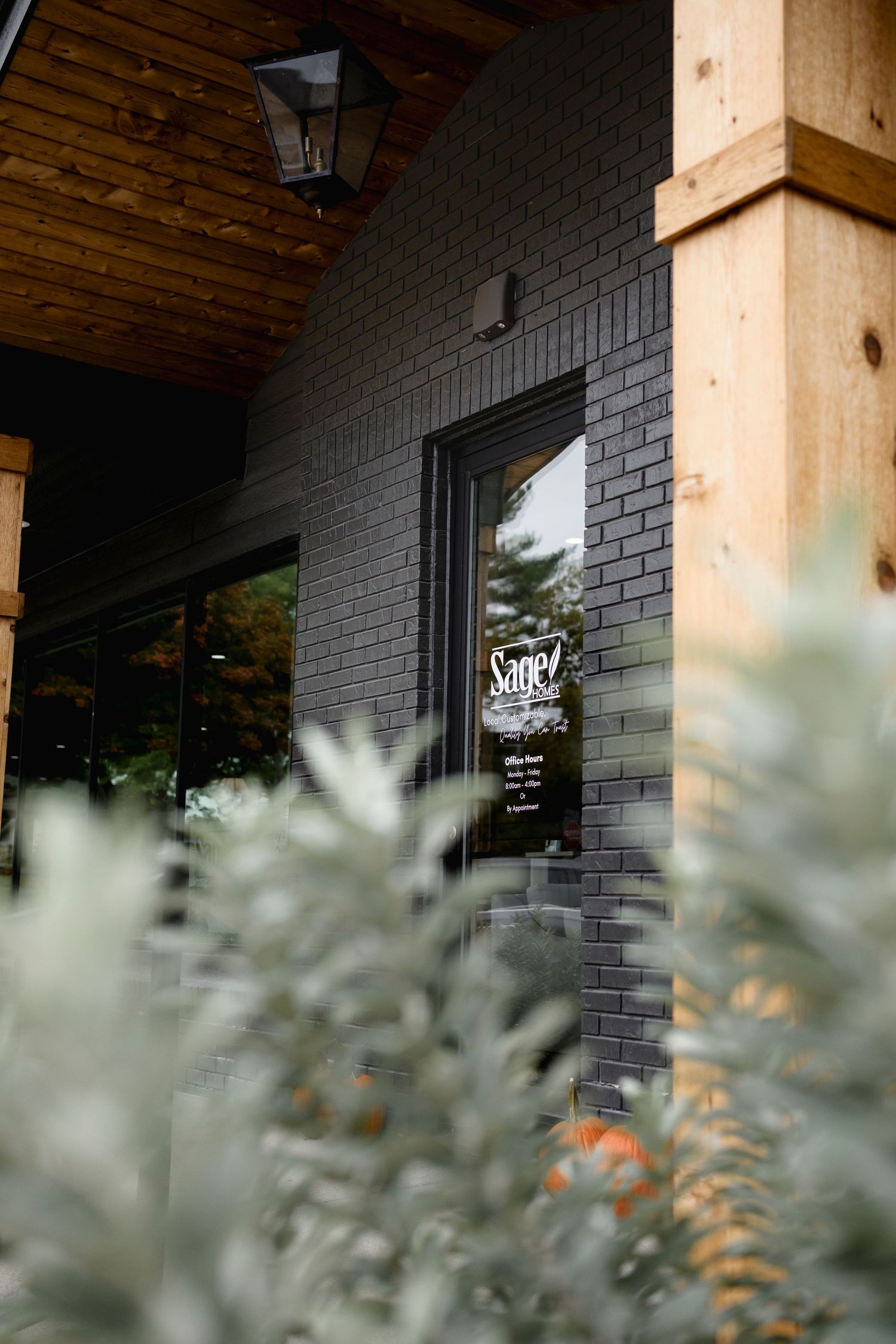 Exterior of Sage restaurant with dark brick walls, wood accents, and lush greenery framing the entrance door.