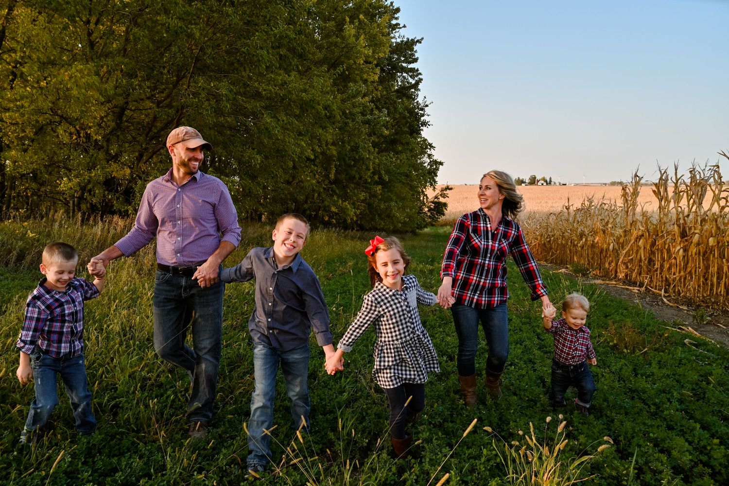 Family of six holding hands walking along a sunny farm field at sunset.