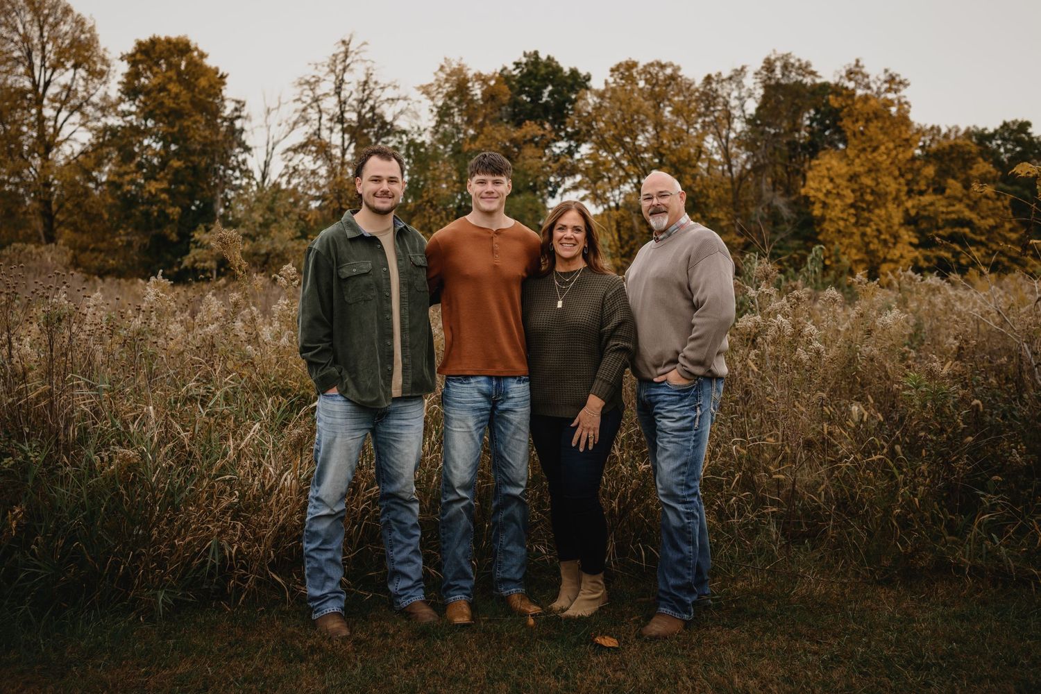 Family of four smiling together in a fall outdoor setting with golden foliage.