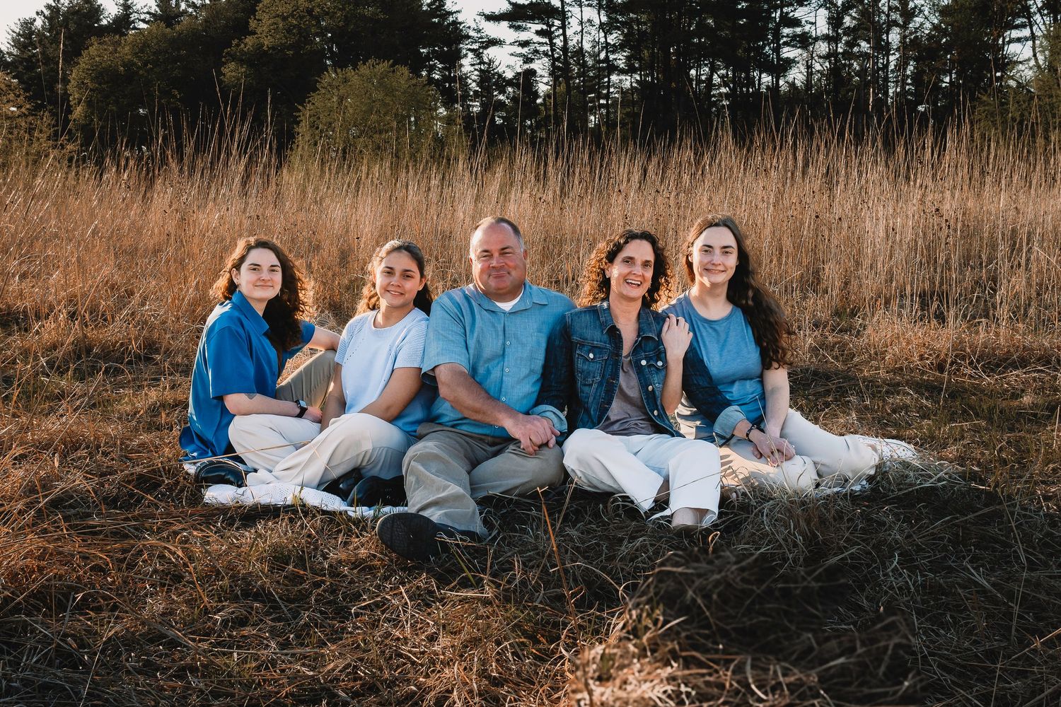 Family of five sitting together in a golden grass field during sunset.