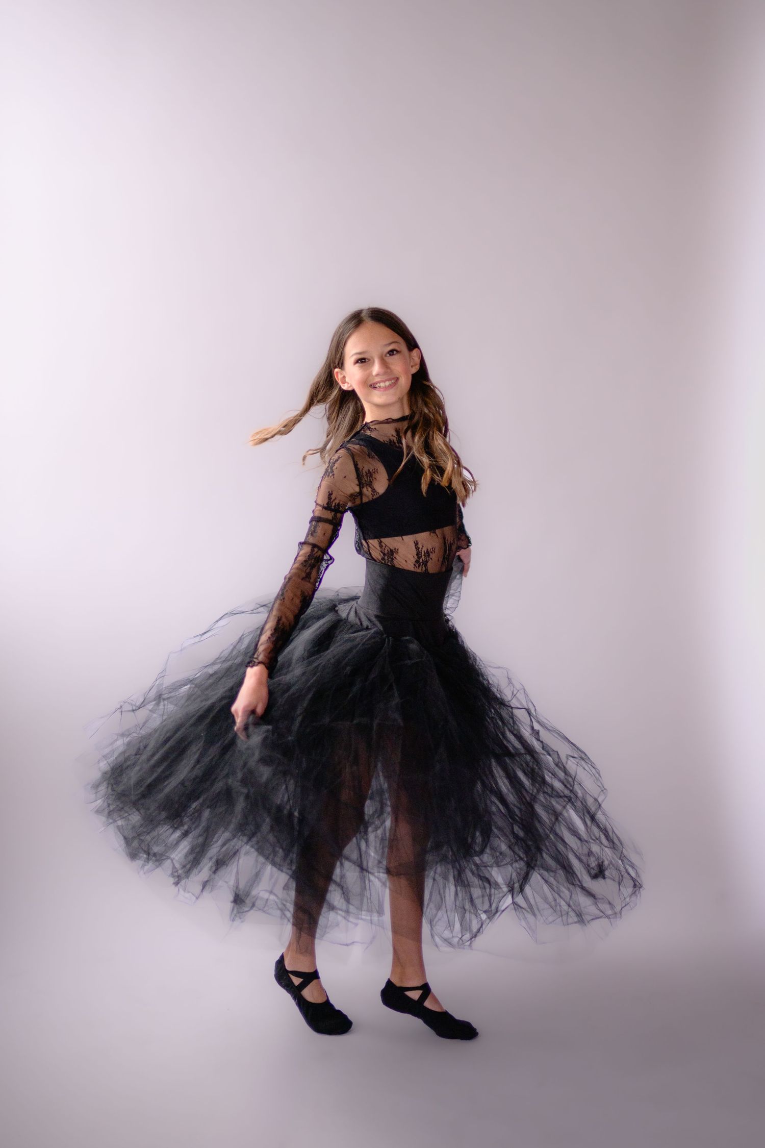 Young girl twirling in a black lace and tulle dance costume against a white background.
