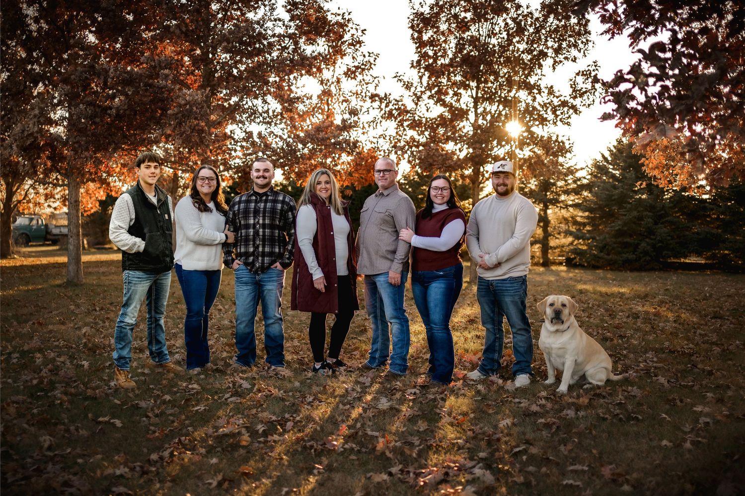 Large family group portrait with dog among autumn trees with golden foliage at sunset.